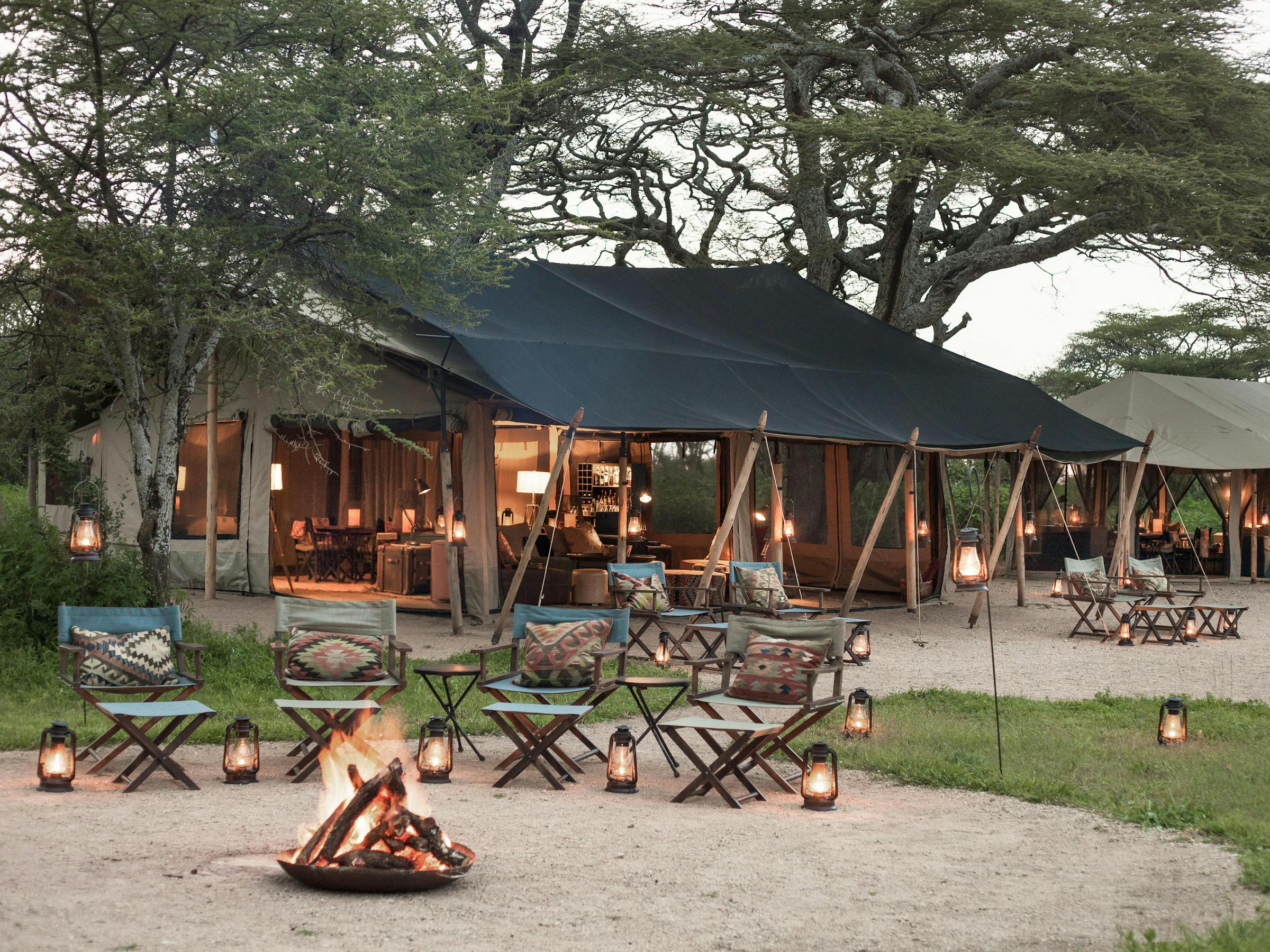 Canvas tents and a shaded lounge area sit on open plains, with wooden decks and chairs facing outward.