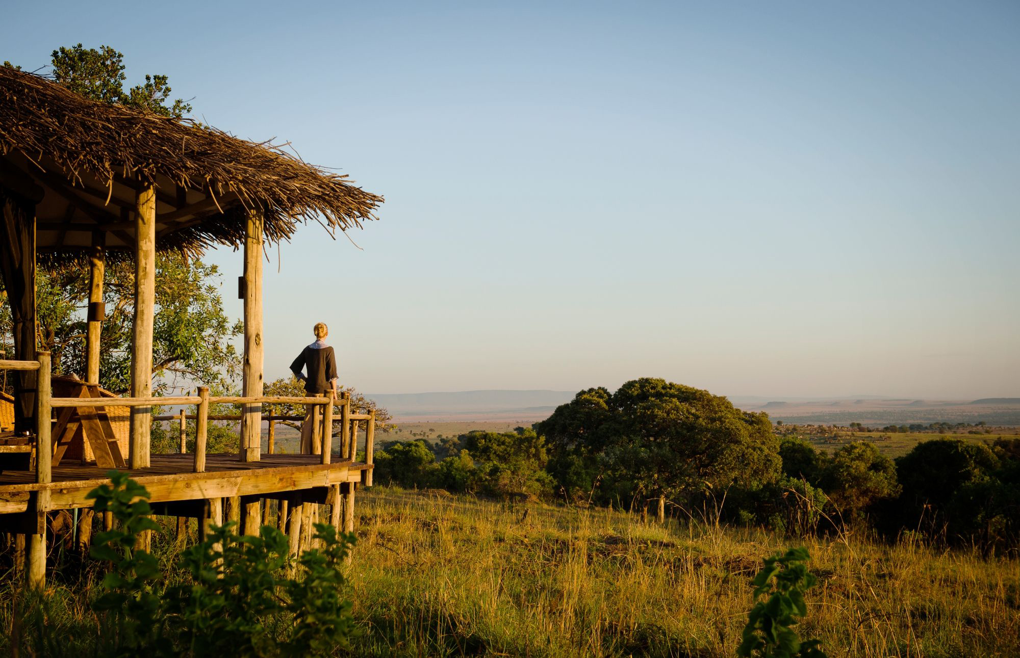 Private wooden deck with lounge chairs looks out over open plains, framed by a thatched roof and shade.