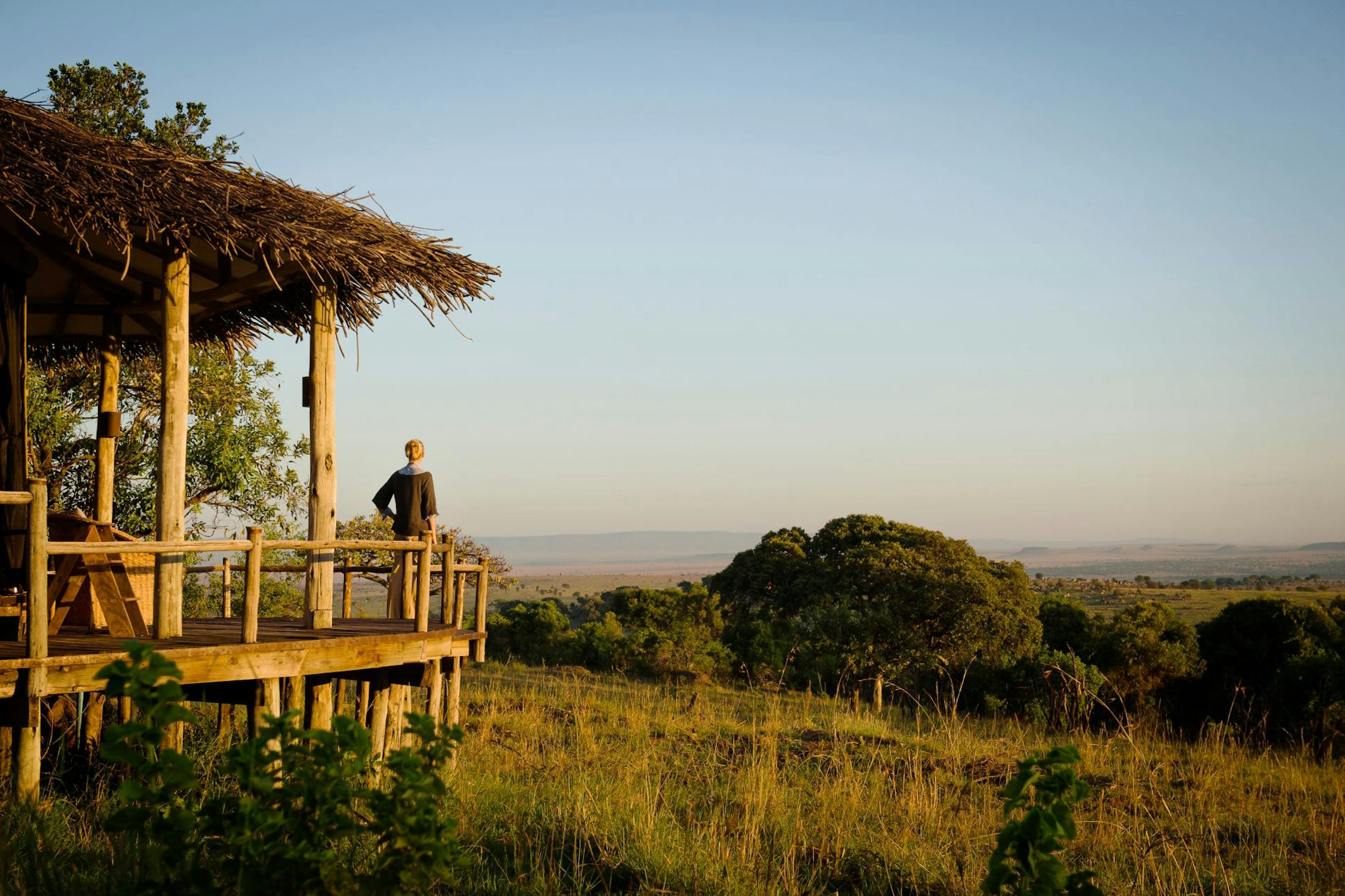 Private wooden deck with lounge chairs looks out over open plains, framed by a thatched roof and shade.