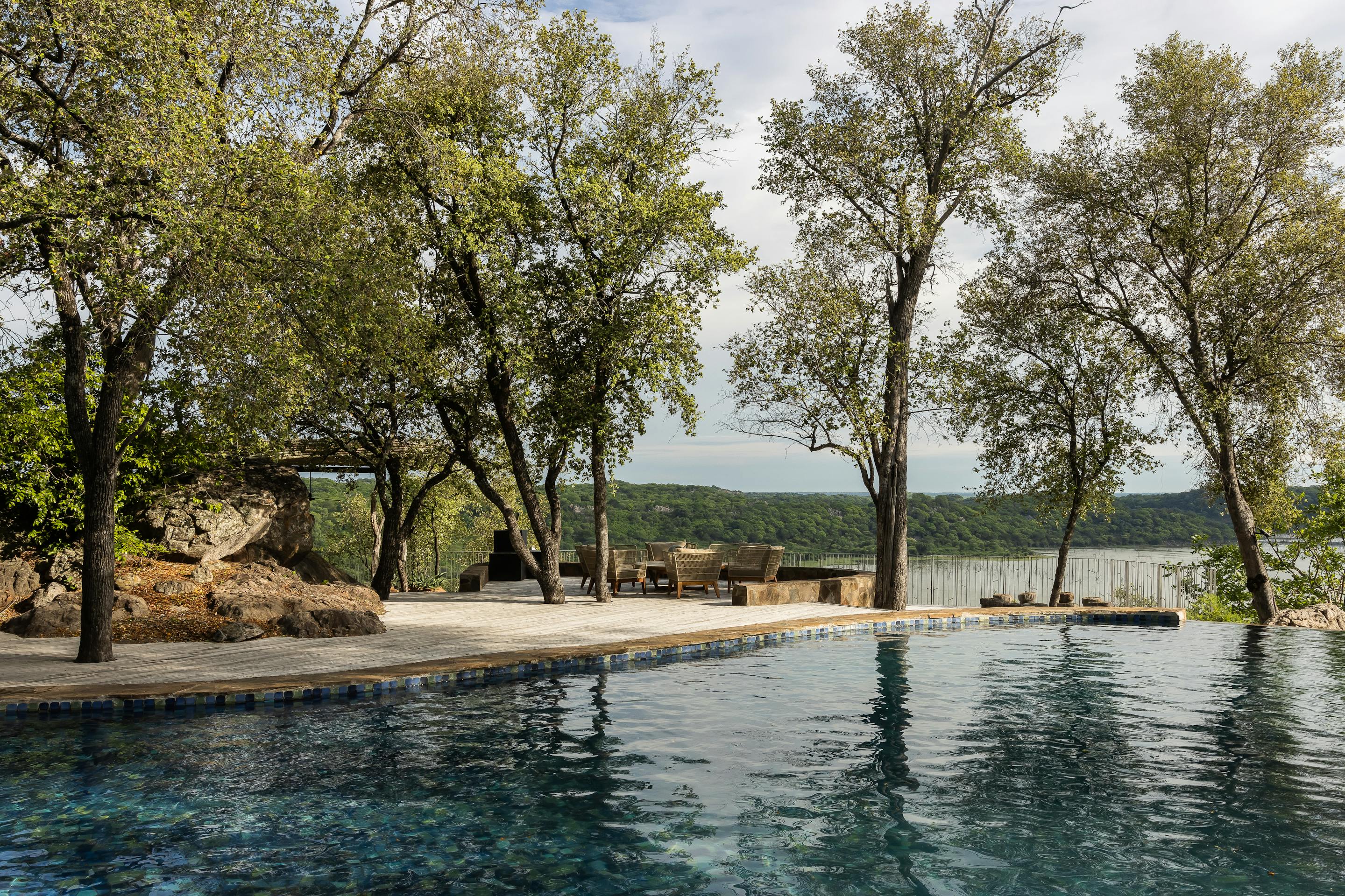 Infinity pool overlooks forested hills at sunset, with loungers on the deck and soft light on the water.