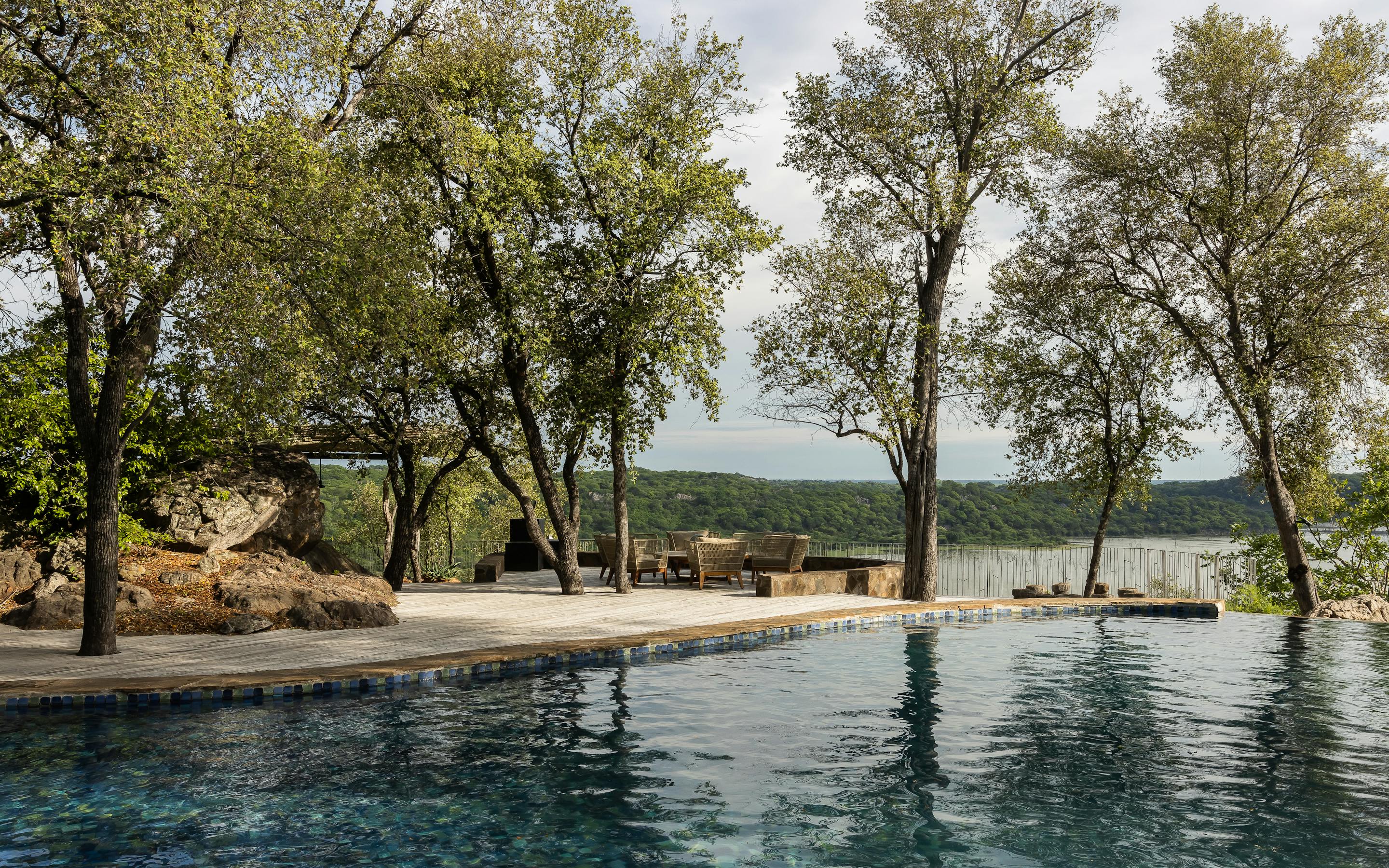 Infinity pool overlooks forested hills at sunset, with loungers on the deck and soft light on the water.