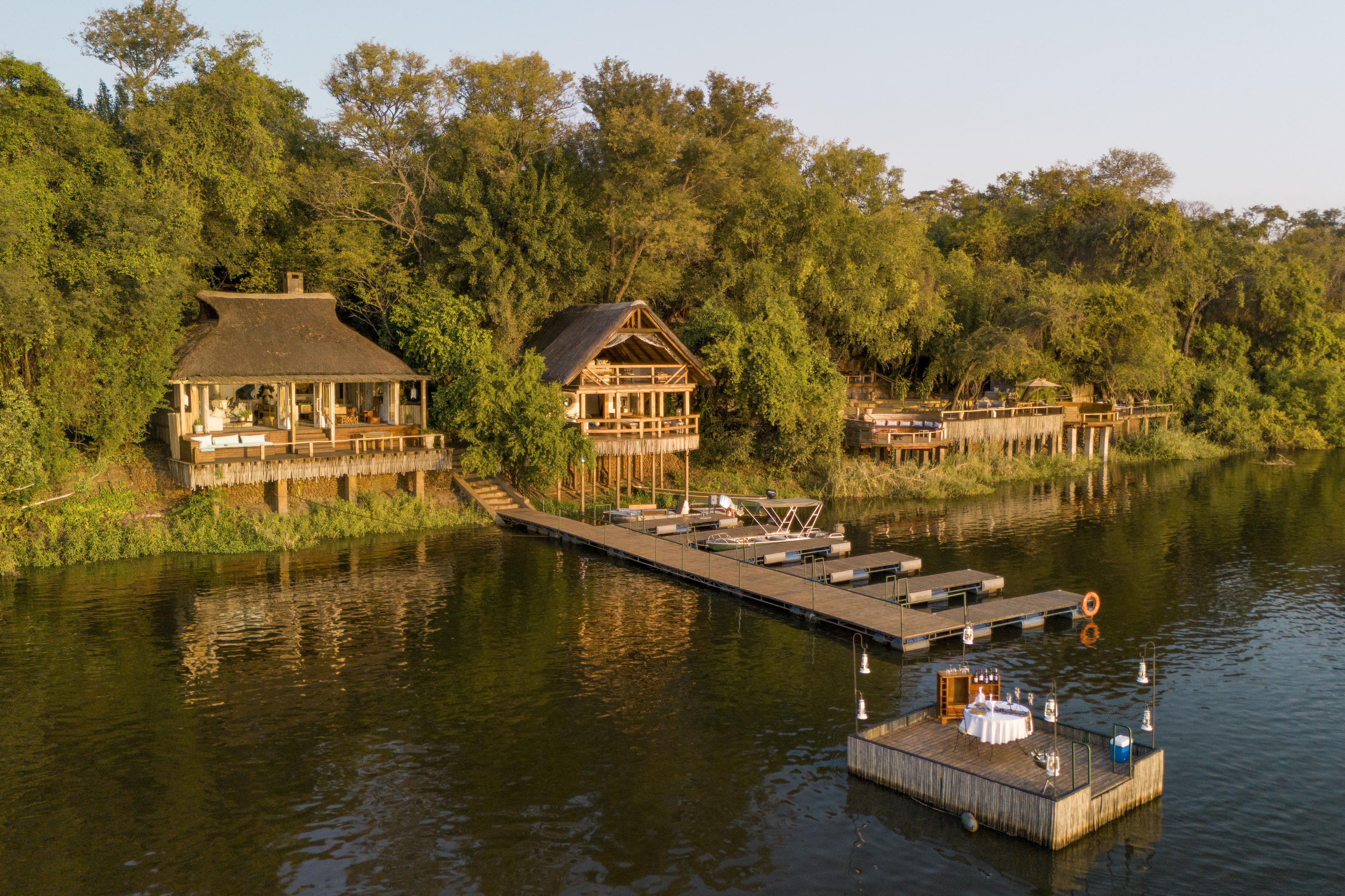 Riverside lodge suites overlook calm water, with a wooden deck and a small boat moored along the green riverbank.