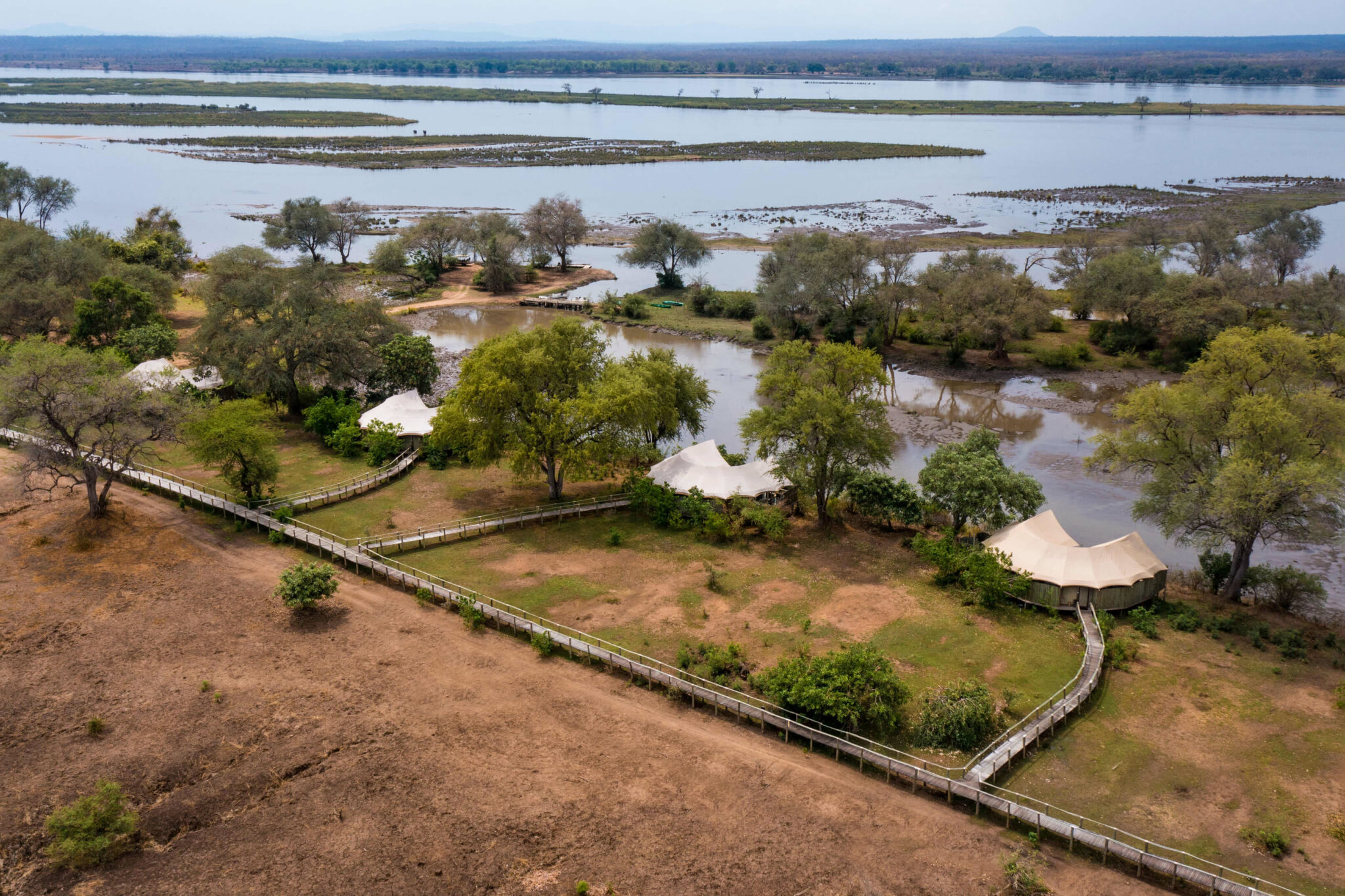 An aerial view shows braided river channels and green islands, with sandy banks and distant hills under blue haze.