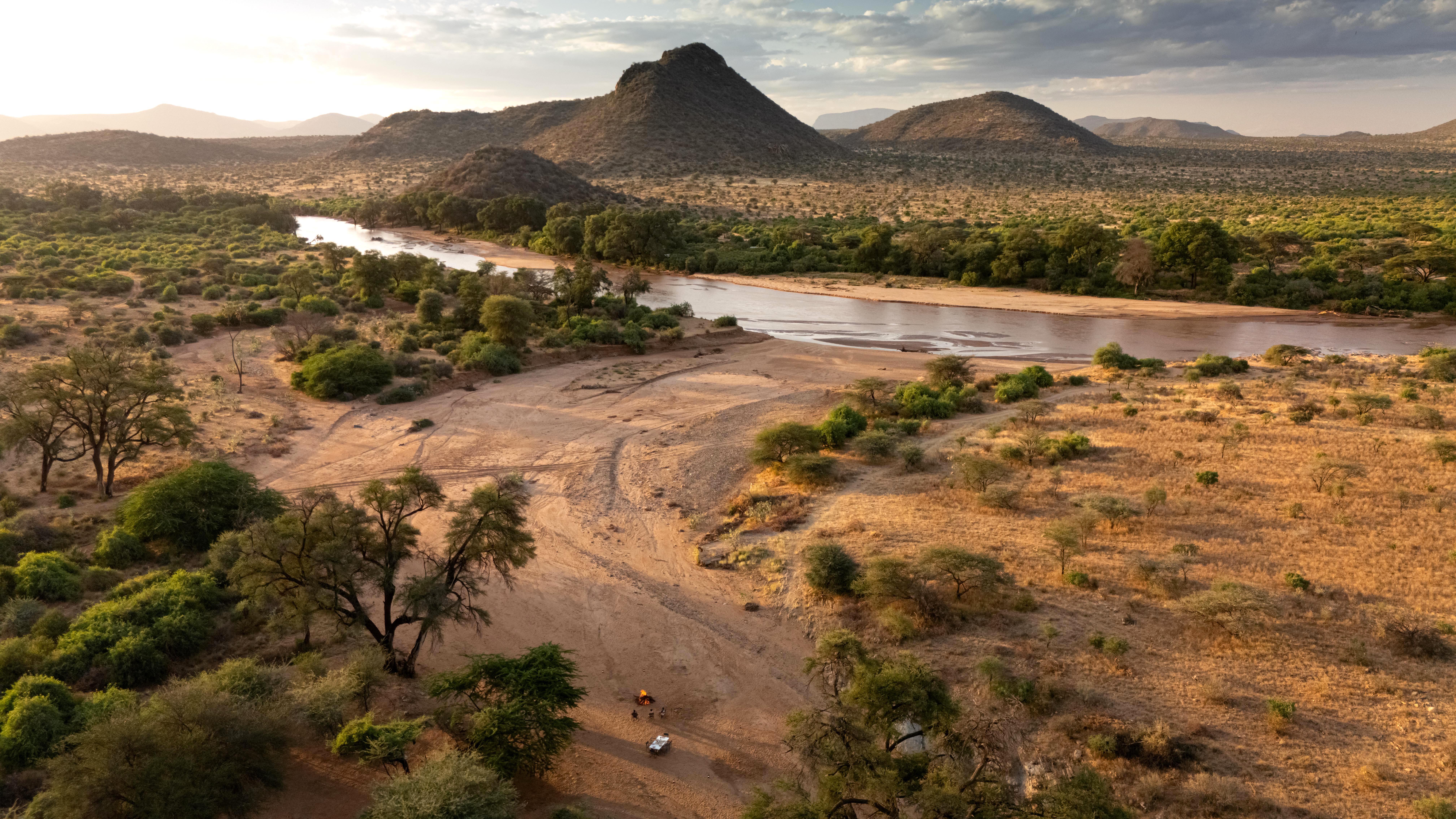 Aerial view of a winding river cutting through dry savanna and hills, with scattered trees along the banks.