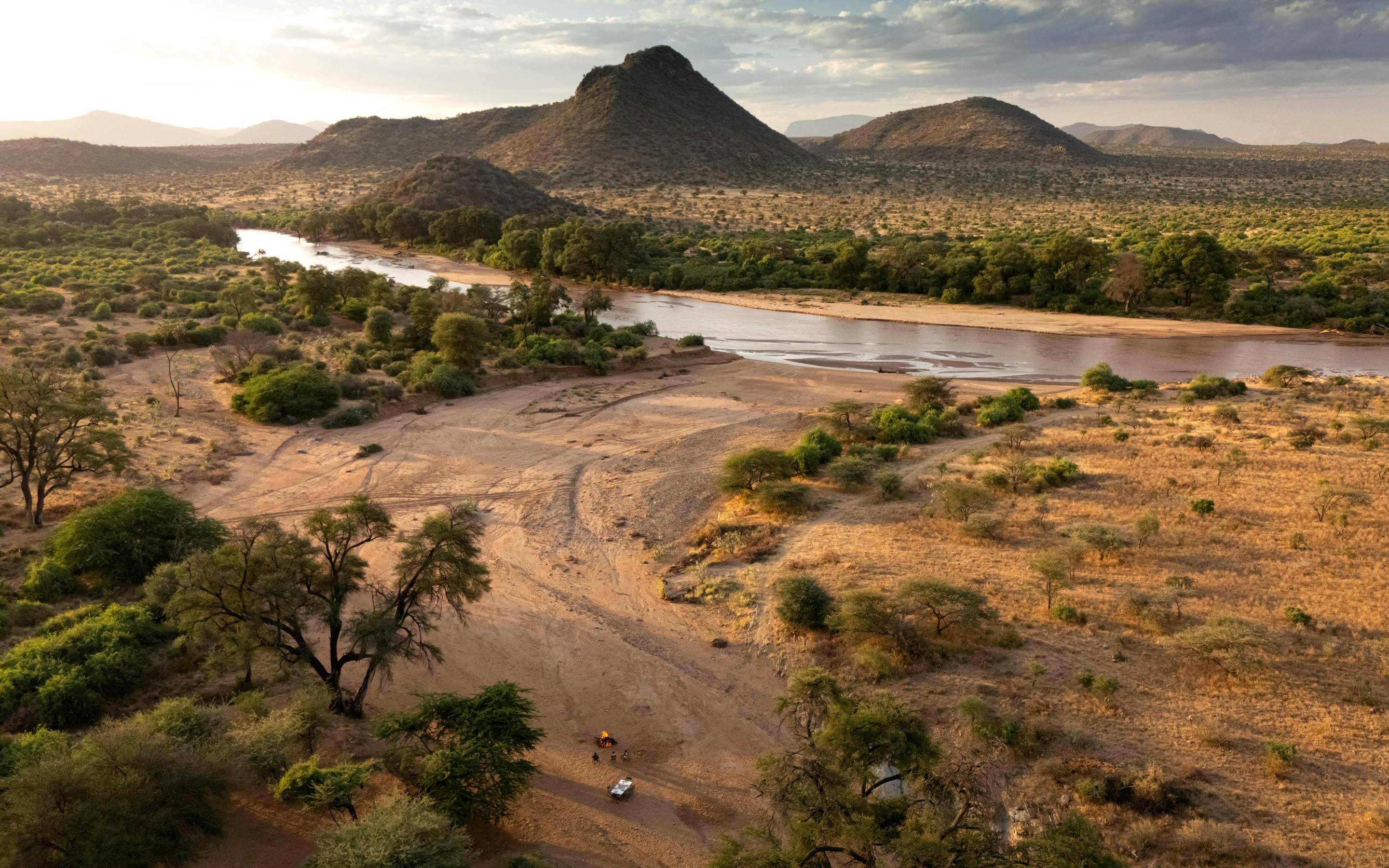 Aerial view of a winding river cutting through dry savanna and hills, with scattered trees along the banks.