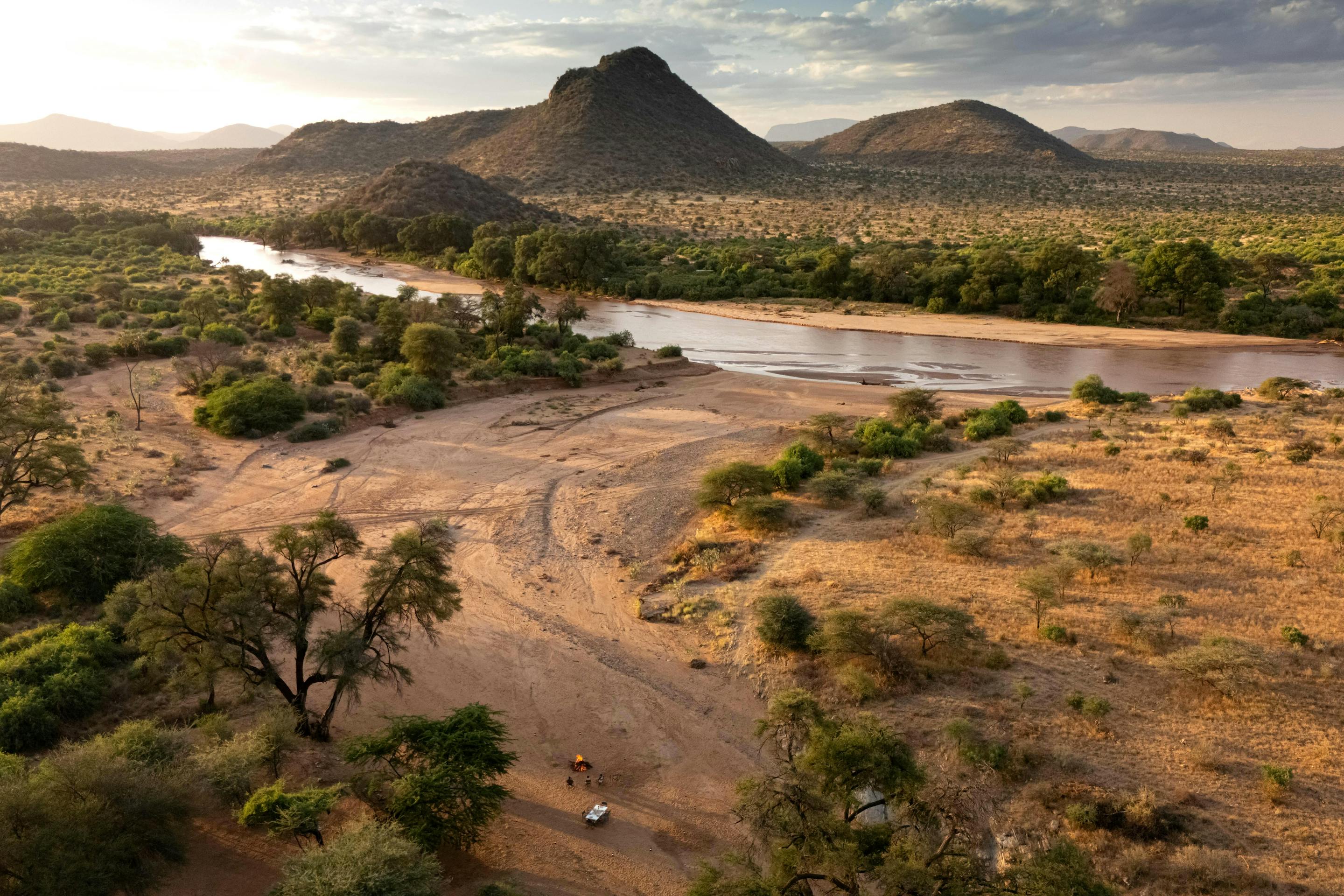 Aerial view of a winding river cutting through dry savanna and hills, with scattered trees along the banks.