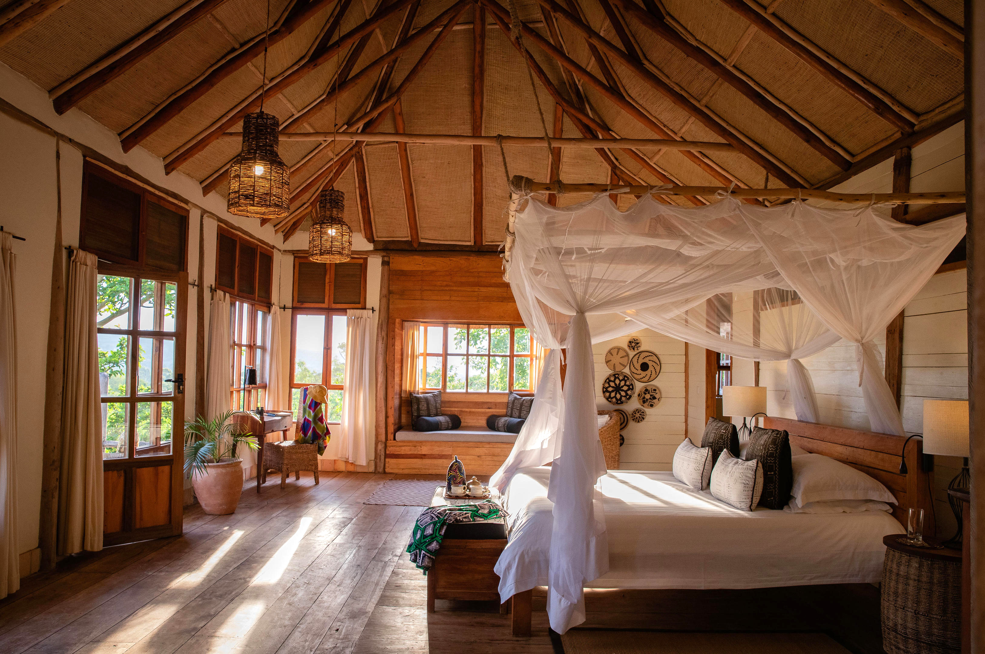 A neatly made bed sits beneath a white mosquito net inside a canvas tent room, with soft daylight at the windows.