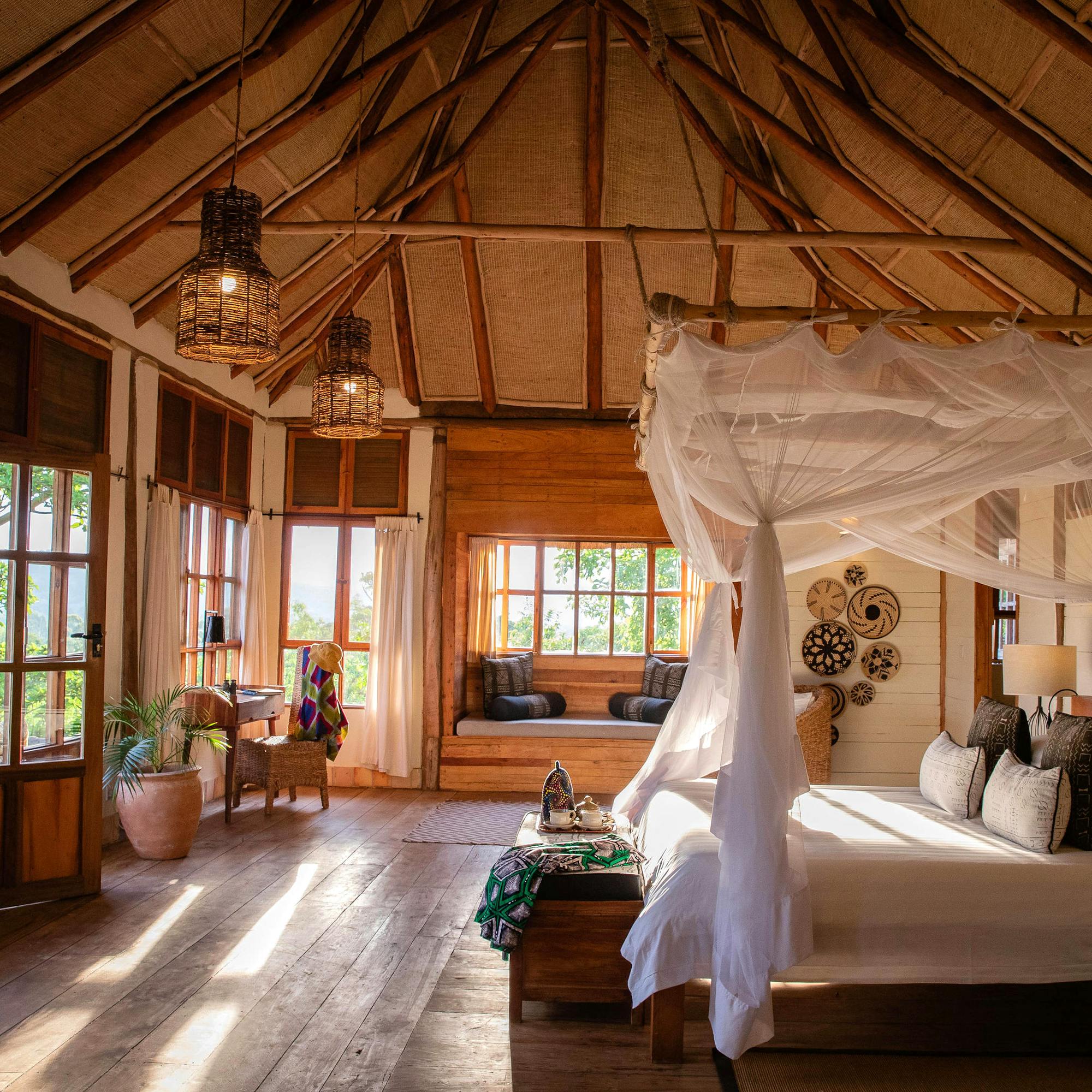 A neatly made bed sits beneath a white mosquito net inside a canvas tent room, with soft daylight at the windows.