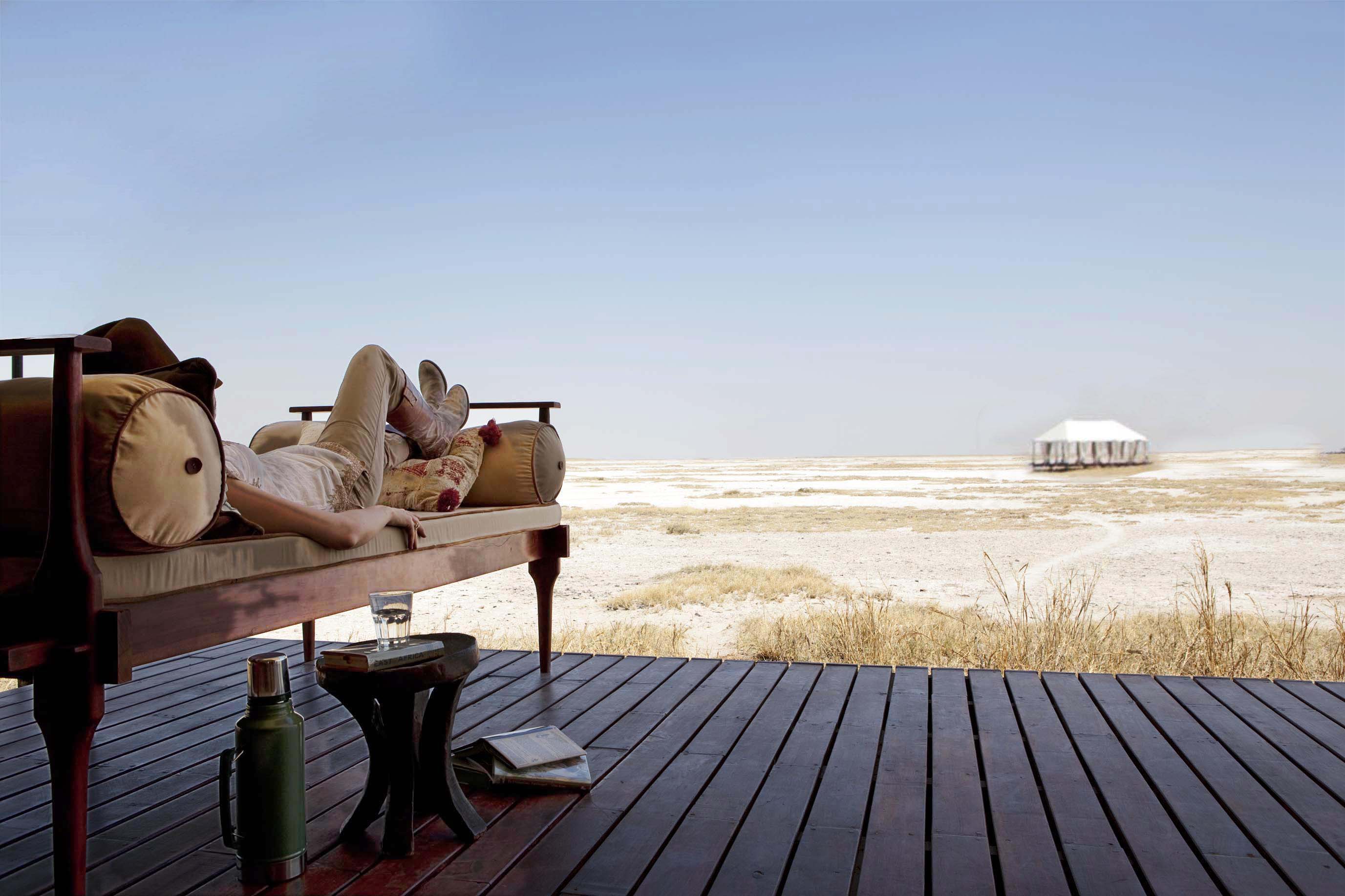 Canvas tent deck with daybeds faces a vast white salt pan, with a lone shade umbrella and distant horizon.