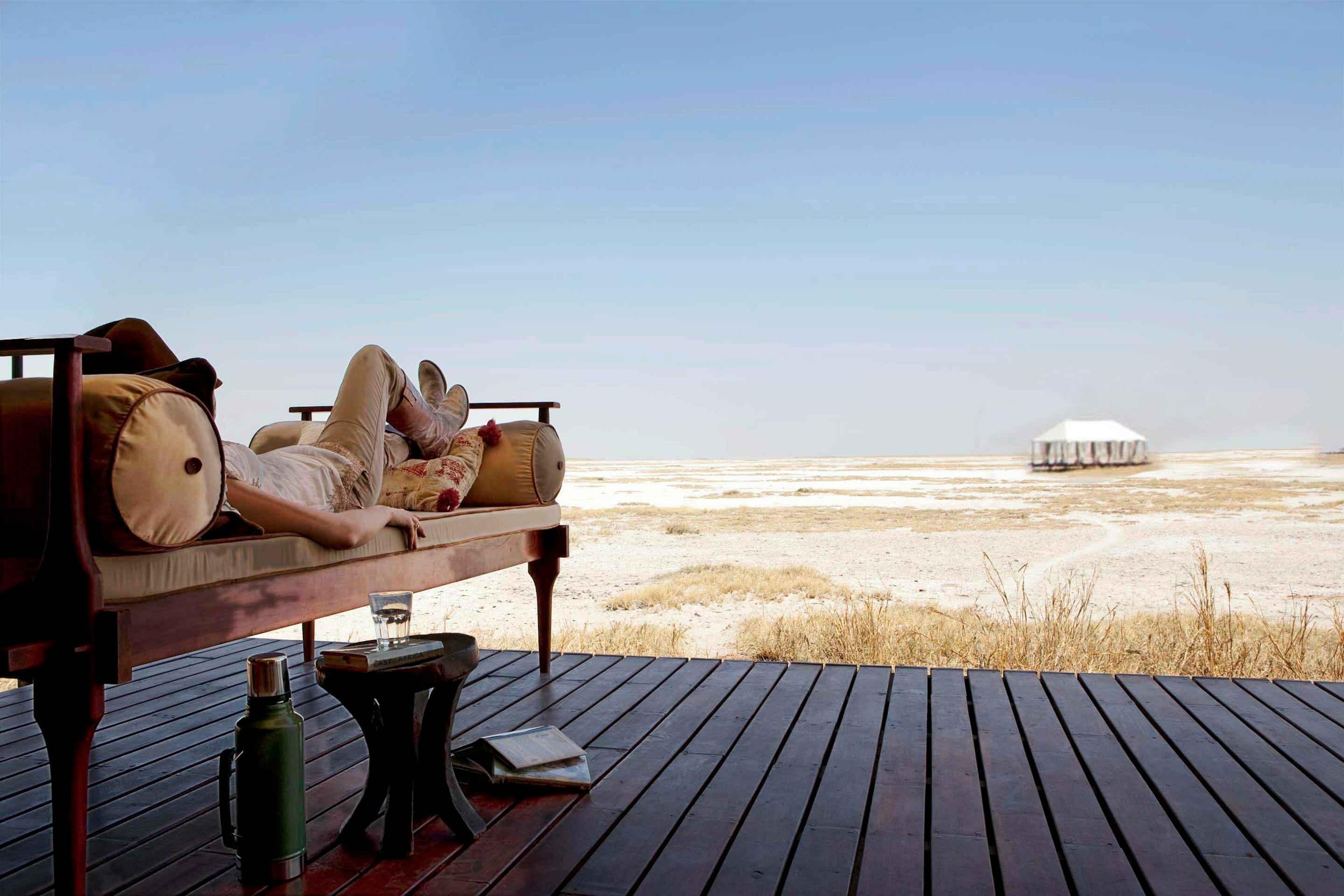 Canvas tent deck with daybeds faces a vast white salt pan, with a lone shade umbrella and distant horizon.