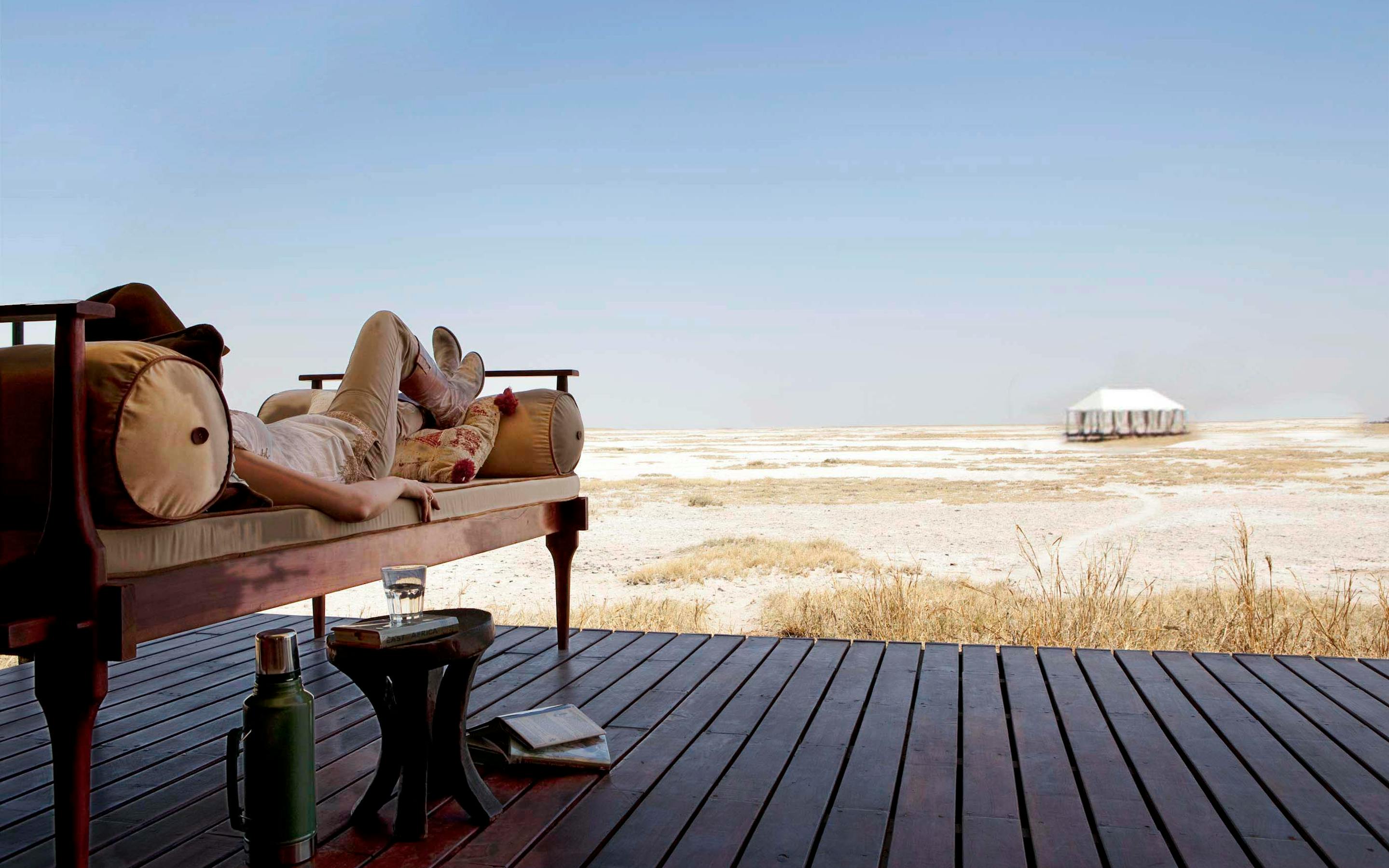Canvas tent deck with daybeds faces a vast white salt pan, with a lone shade umbrella and distant horizon.