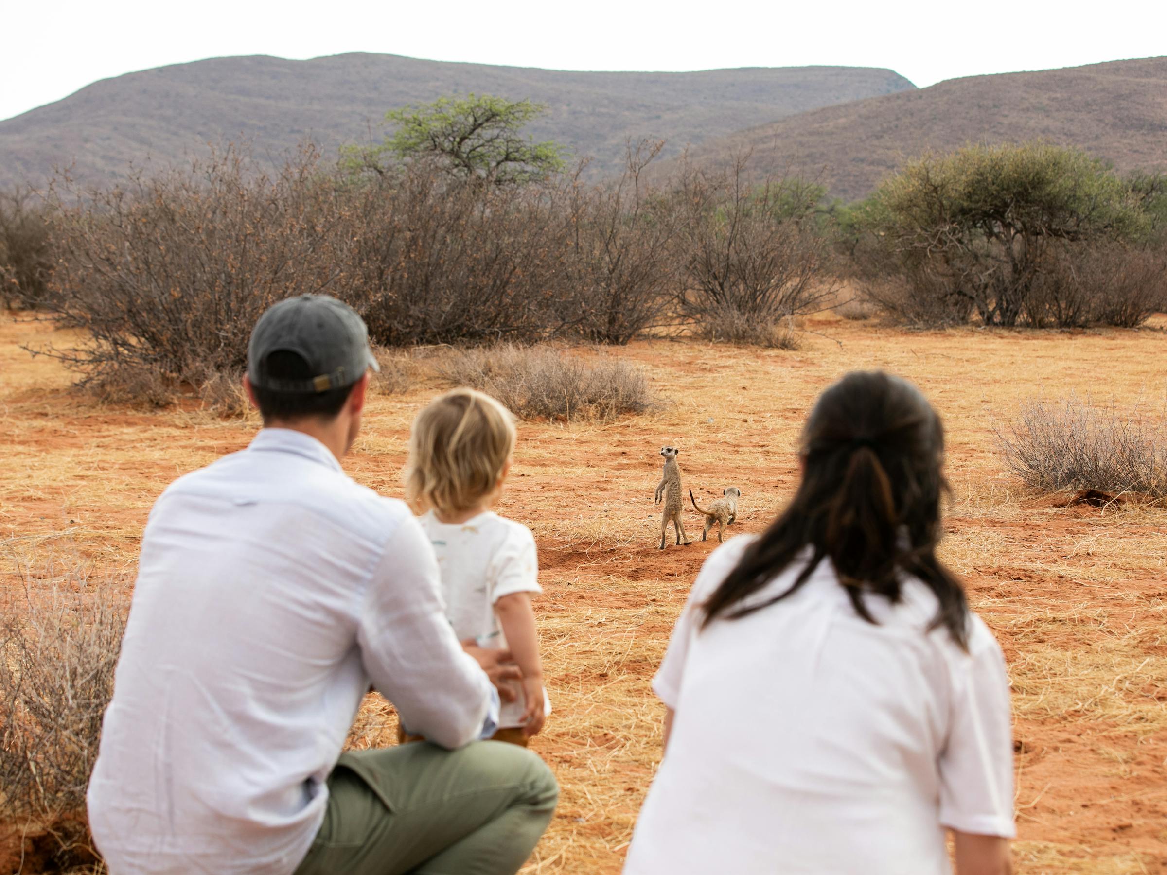 Three people sit on a sandy rise, watching distant hills and open plains in the warm light of late day together.