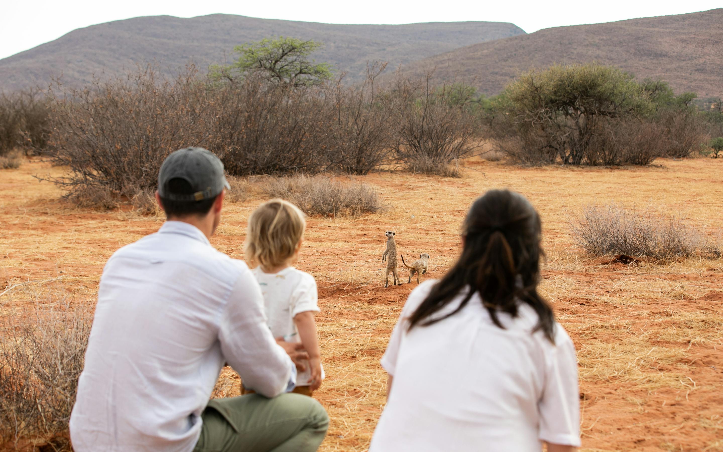 Three people sit on a sandy rise, watching distant hills and open plains in the warm light of late day together.