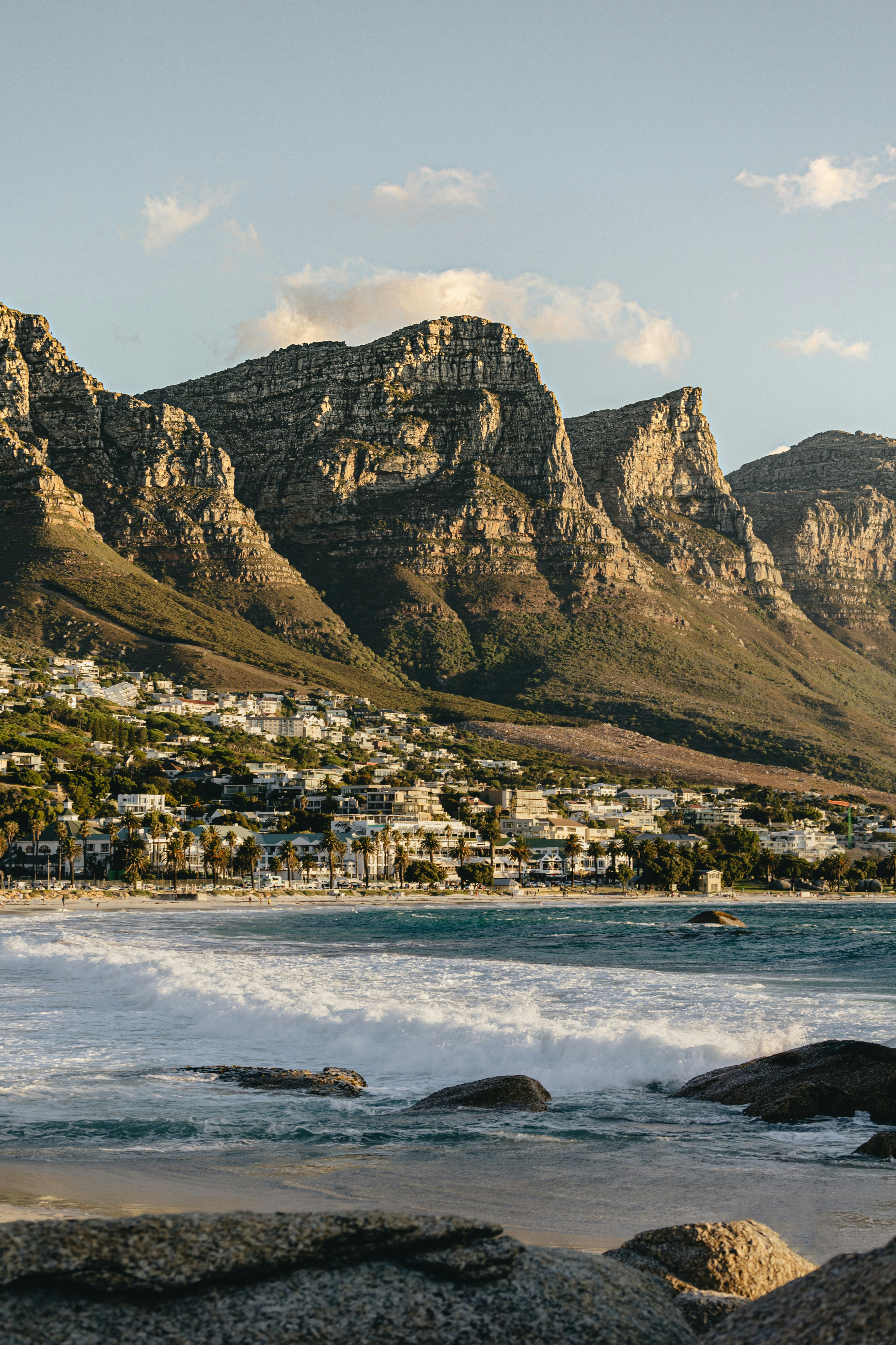 Coastal city spreads along a blue bay below a flat-topped mountain, with boats and buildings in view under a clear sky.