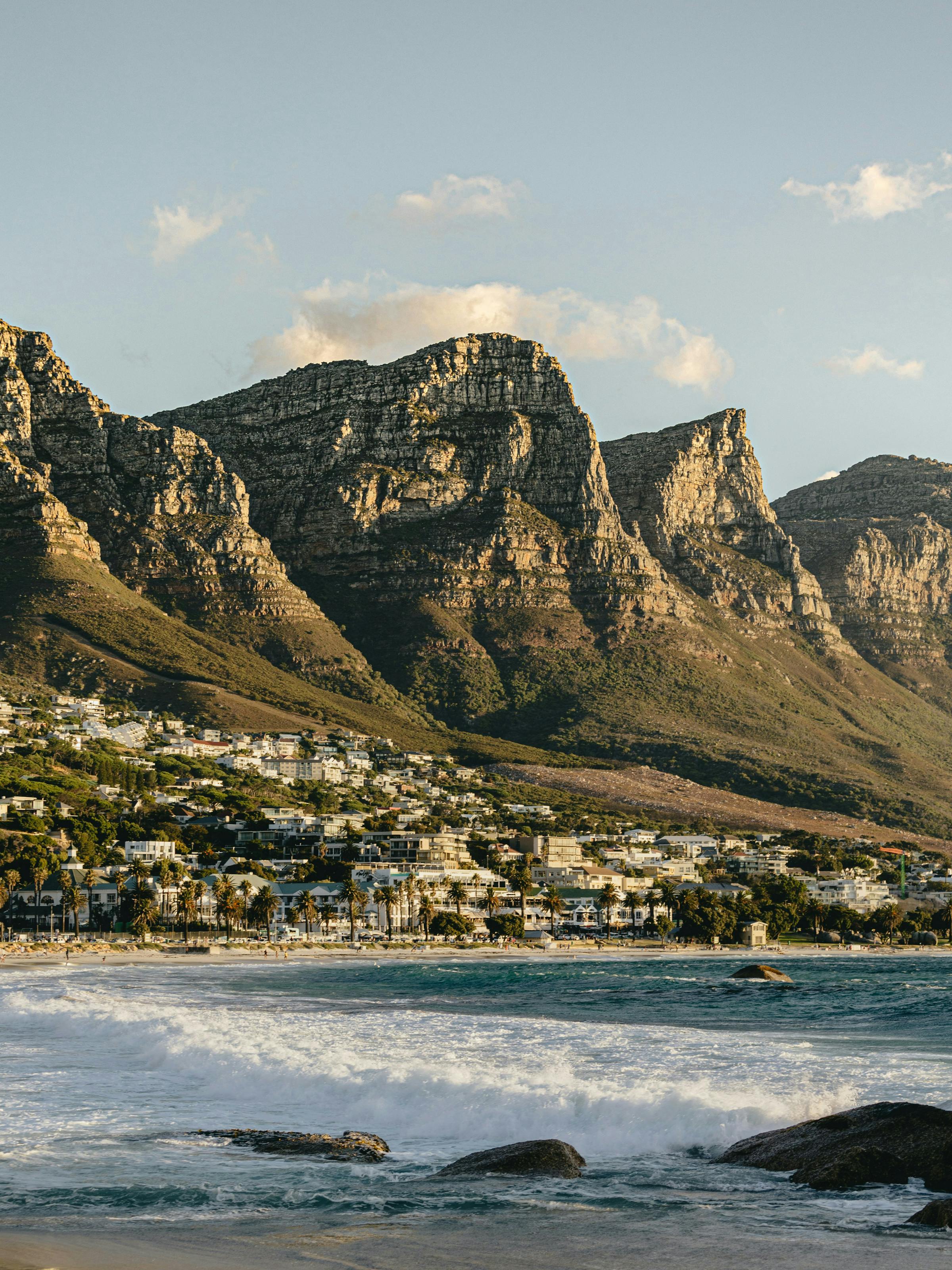 Coastal city spreads along a blue bay below a flat-topped mountain, with boats and buildings in view under a clear sky.