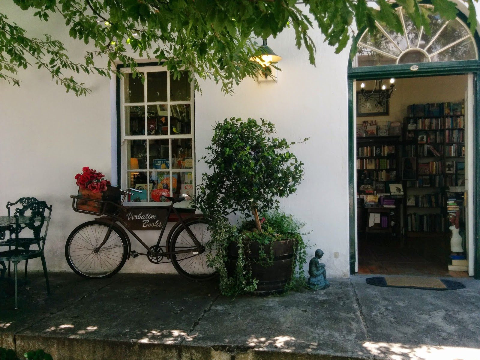 A bicycle leans beside a café doorway framed by vines and potted plants, with chairs set on a stone patio.