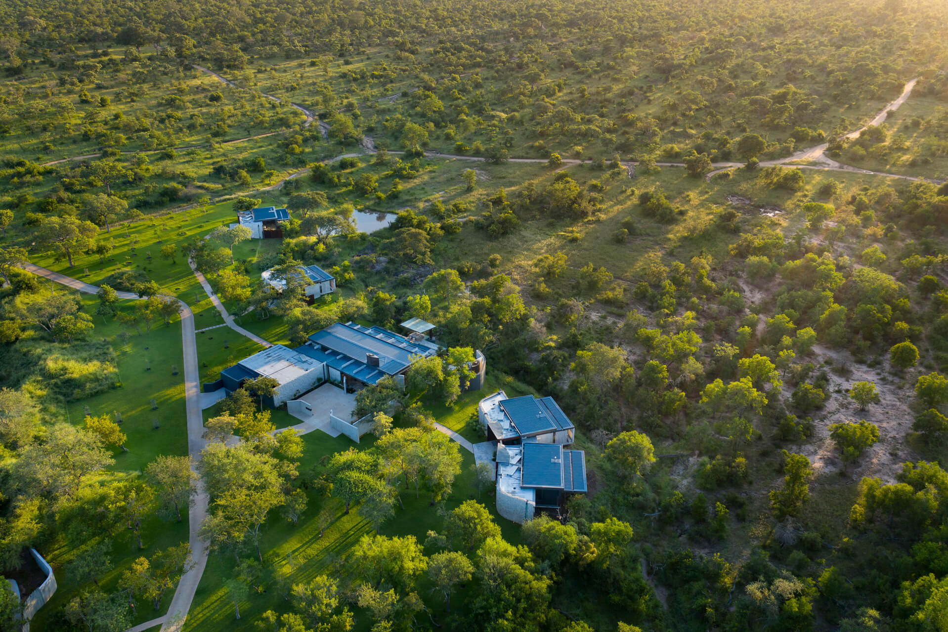 An aerial view shows a lodge compound among trees, with winding driveways and green bush stretching beyond.