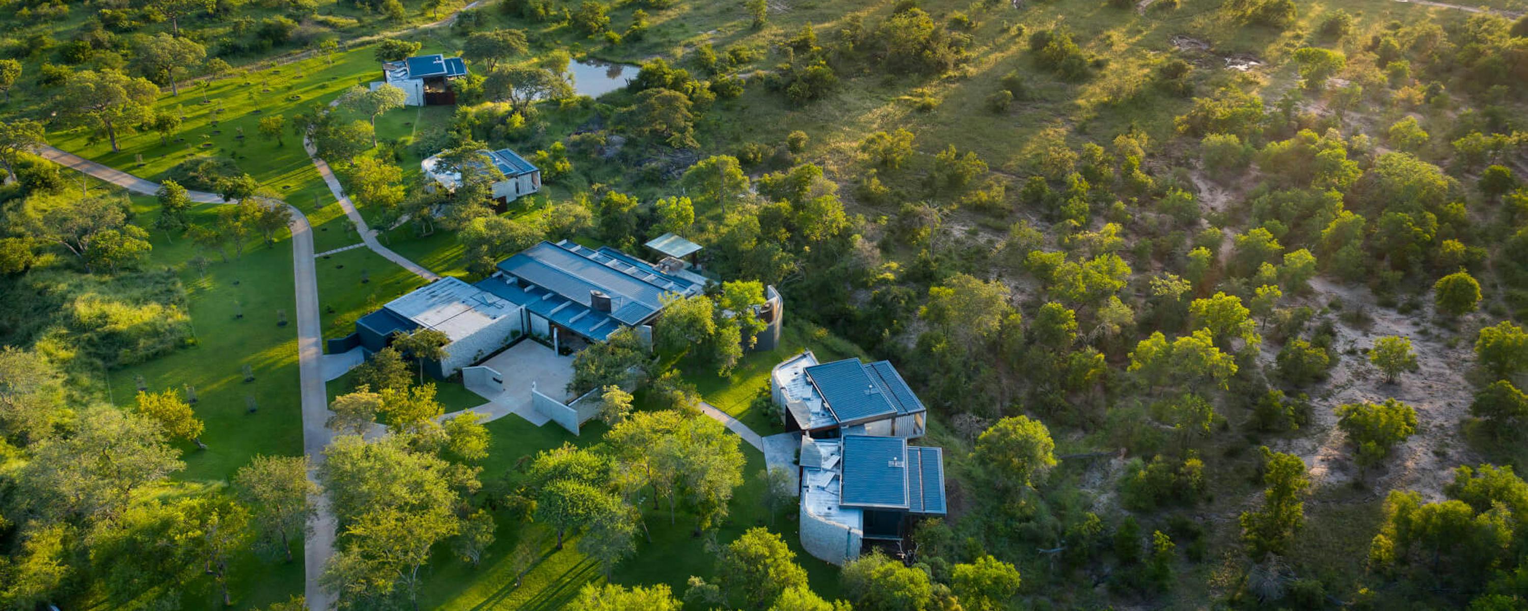 An aerial view shows a lodge compound among trees, with winding driveways and green bush stretching beyond.