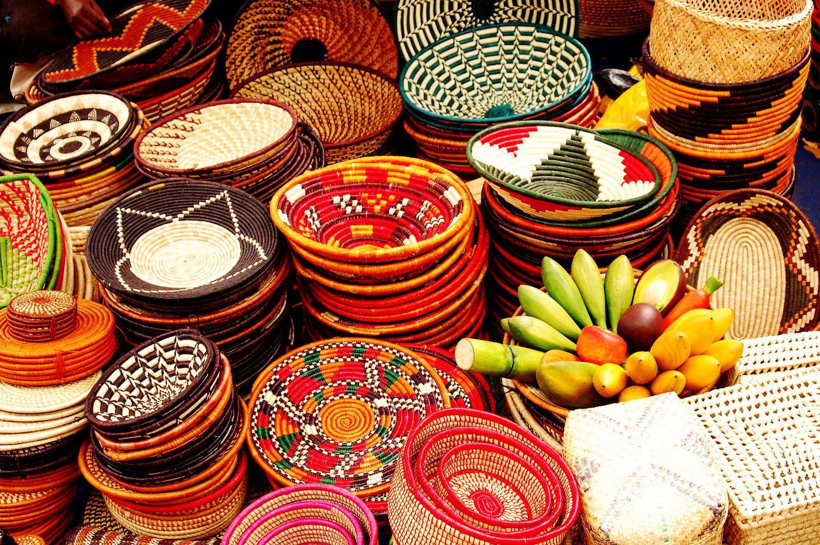 Brightly patterned woven baskets are stacked at a market stall, with bananas and citrus fruit piled nearby.