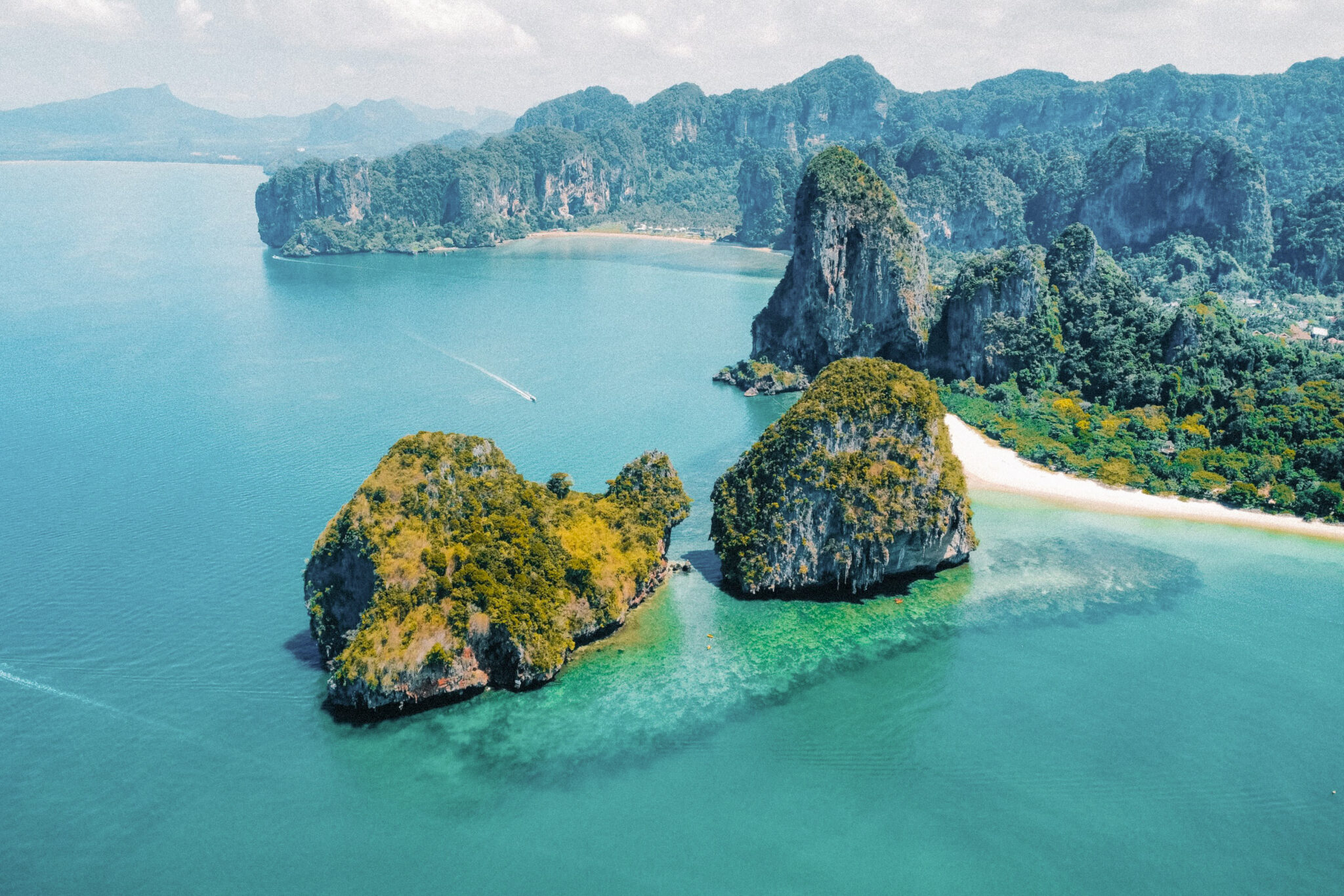 Turquoise water surrounds limestone islets and a white sandbar, with steep green cliffs rising behind the lagoon.