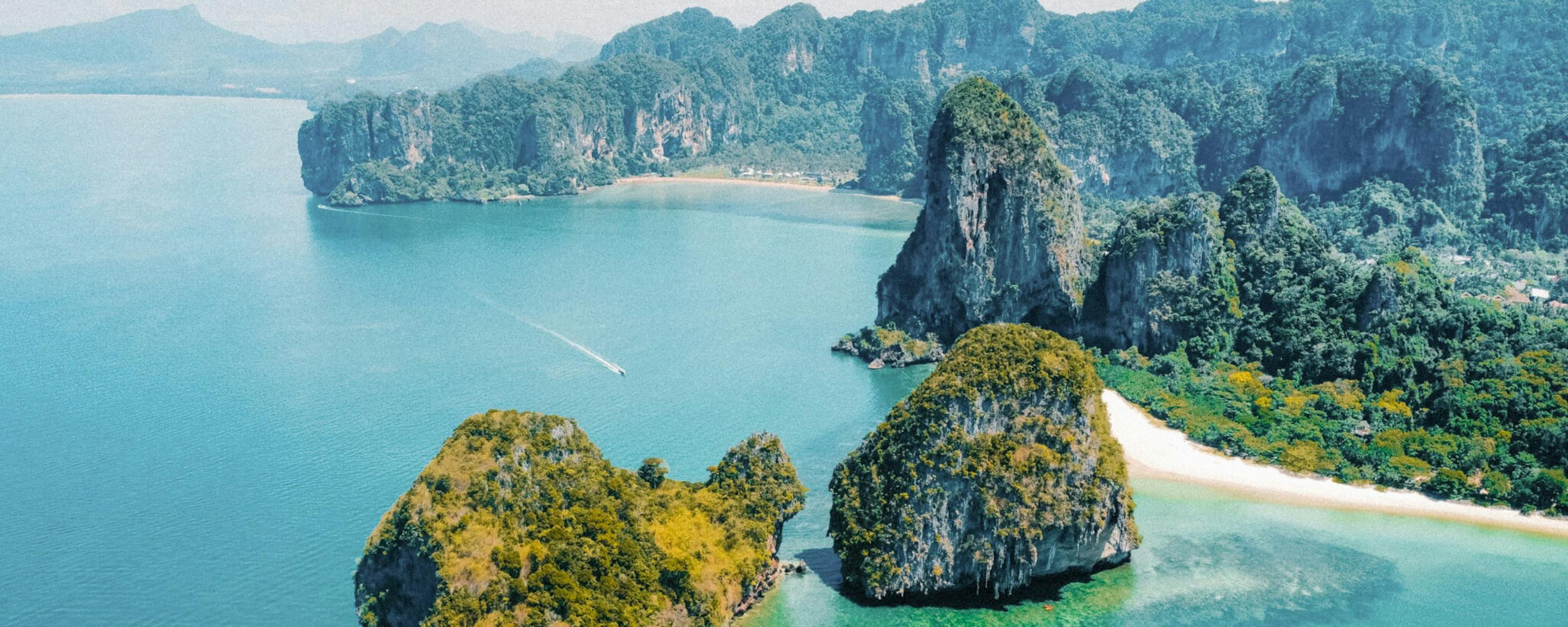 Turquoise water surrounds limestone islets and a white sandbar, with steep green cliffs rising behind the lagoon.
