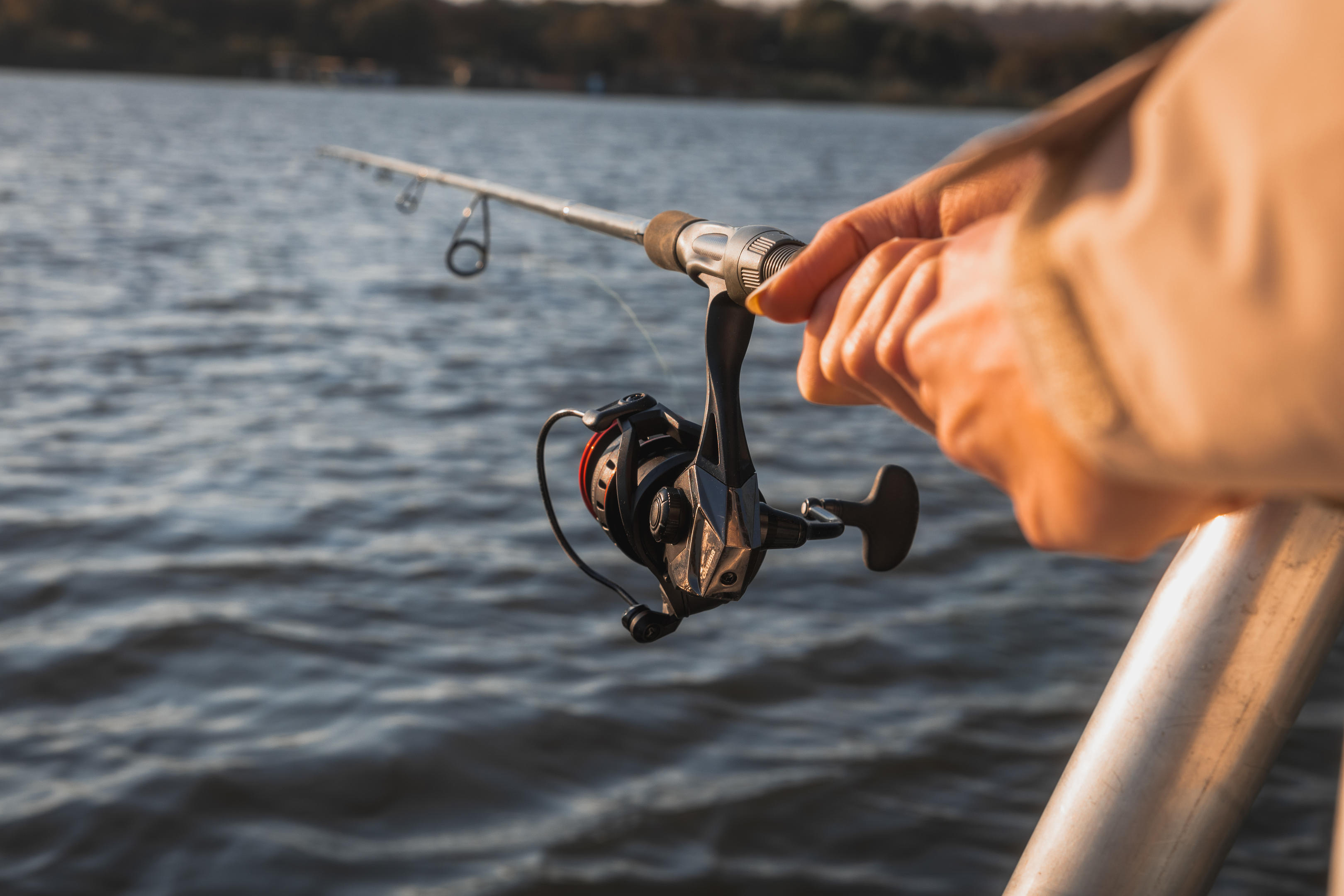 A hand holds a fishing rod over rippling river water, reel and line taut as the lure skims near the surface.