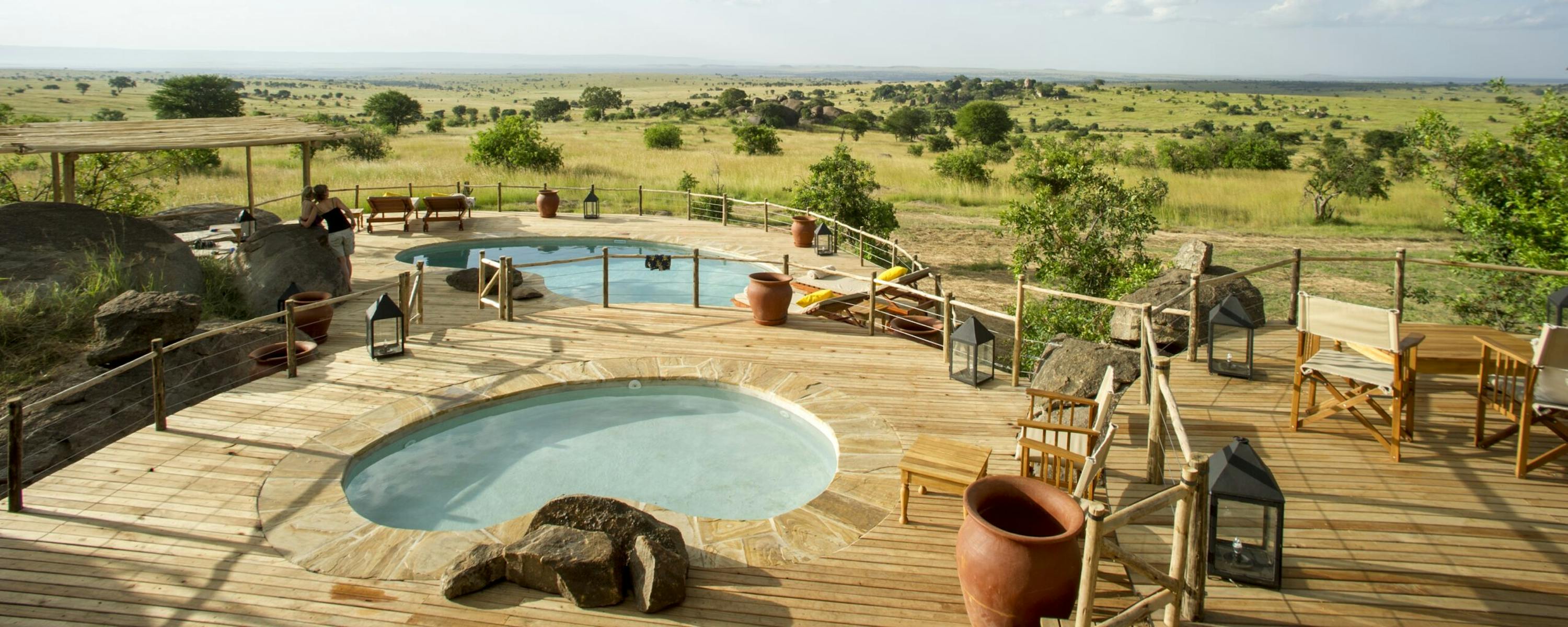 Round plunge pool on a wooden deck faces open plains, with lounge chairs, canvas screens, and big sky clouds.