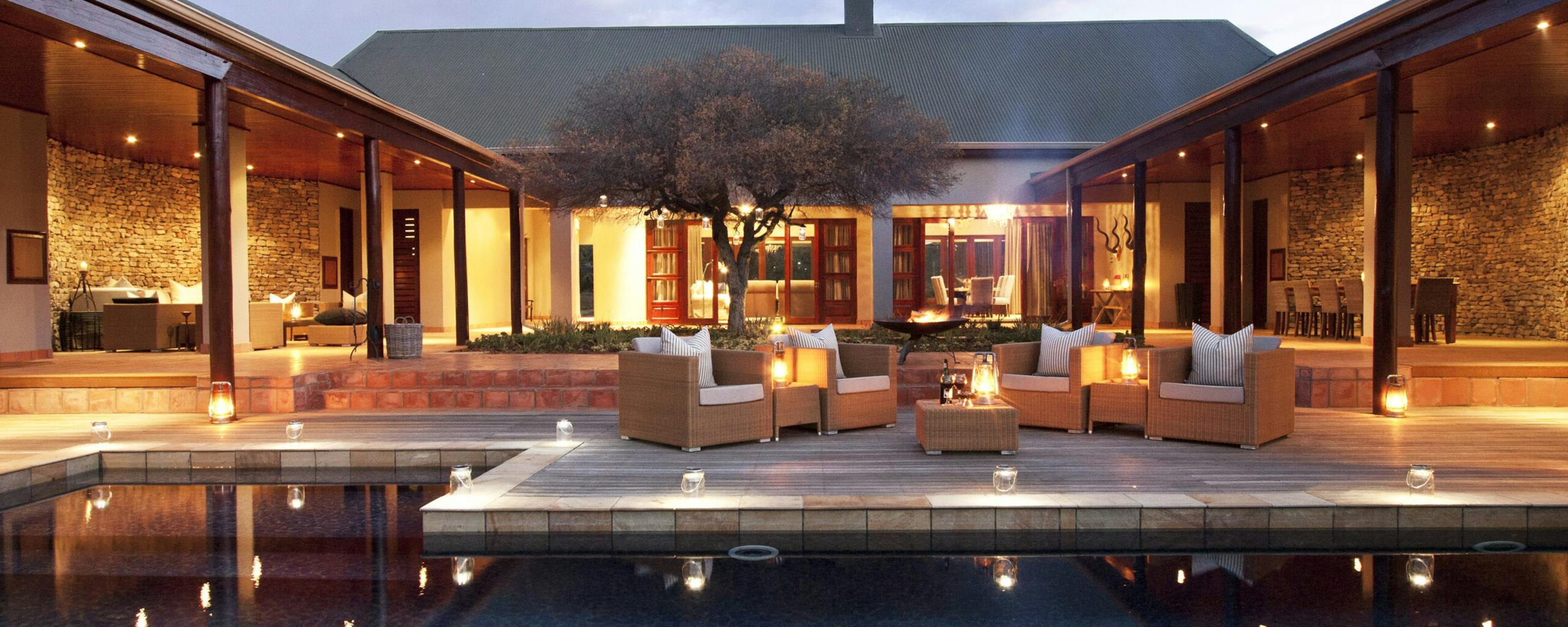Lit courtyard pool reflects a modern lodge, with open-air lounges, stone walls, and warm lantern light at dusk.