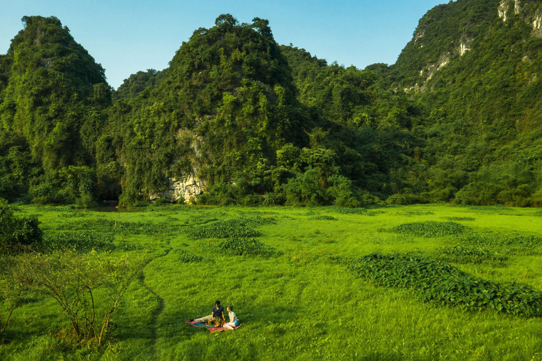 Two people sit and have a picnic below towering limestone karsts beneath a clear sky