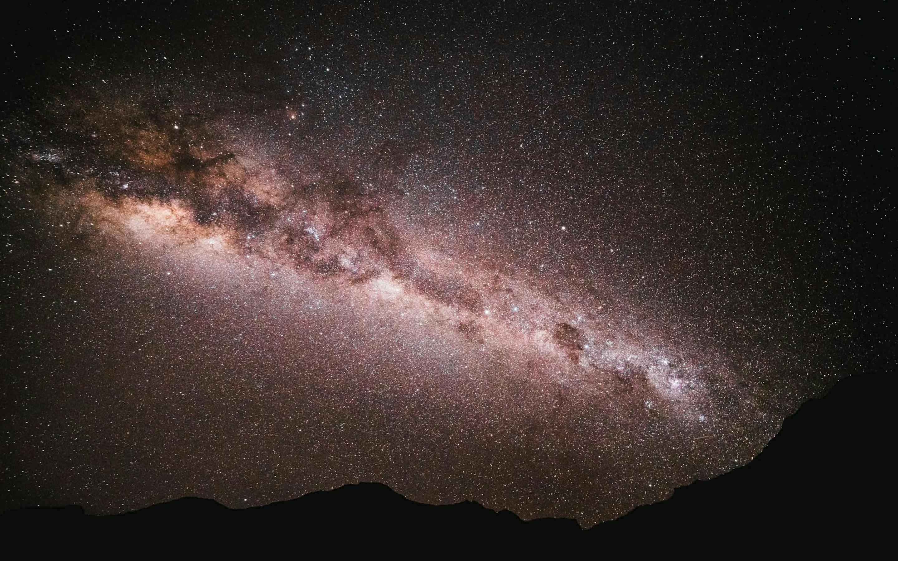 The Milky Way arches across a dark Atacama sky, with dense stars above the low silhouette of distant hills.