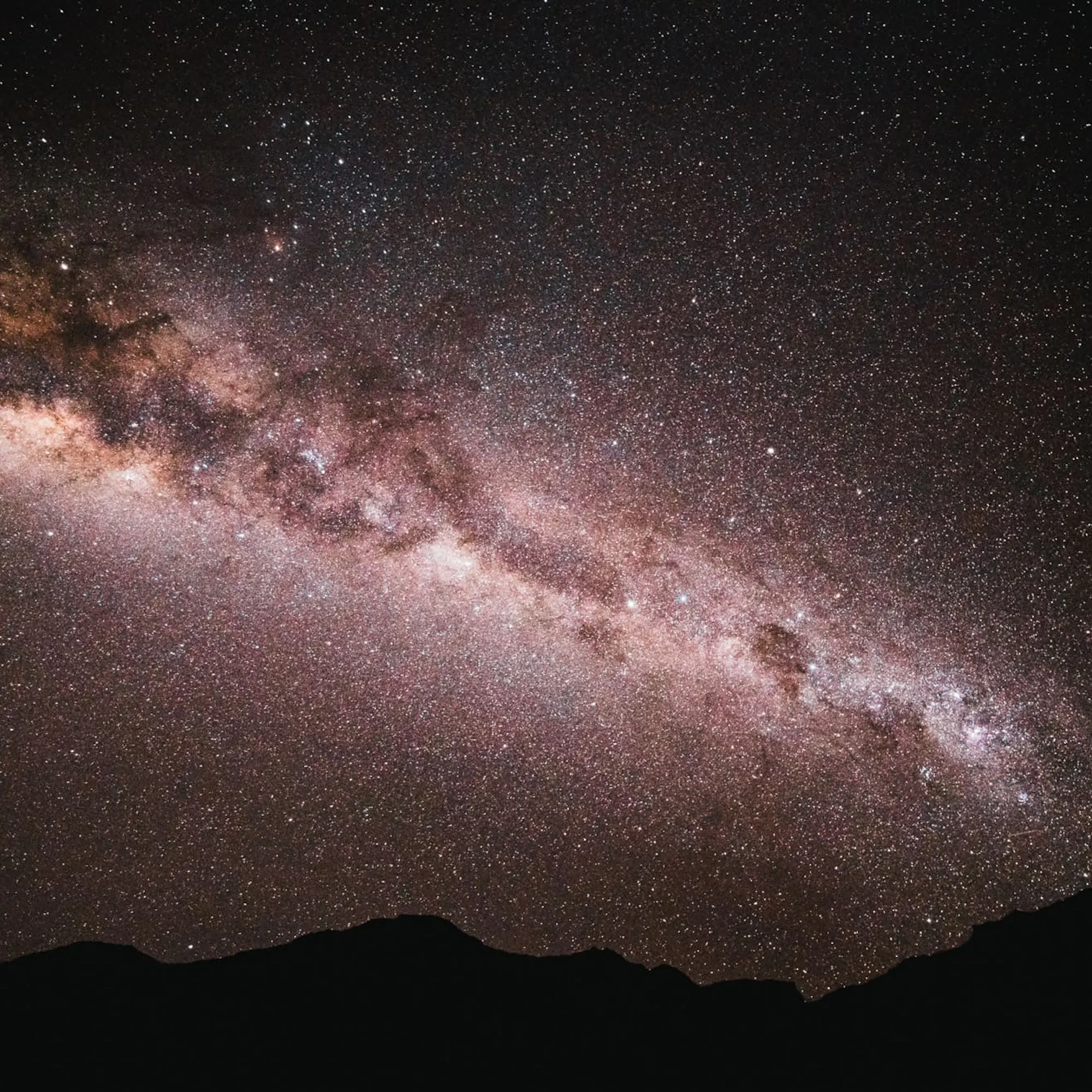The Milky Way arches across a dark Atacama sky, with dense stars above the low silhouette of distant hills.