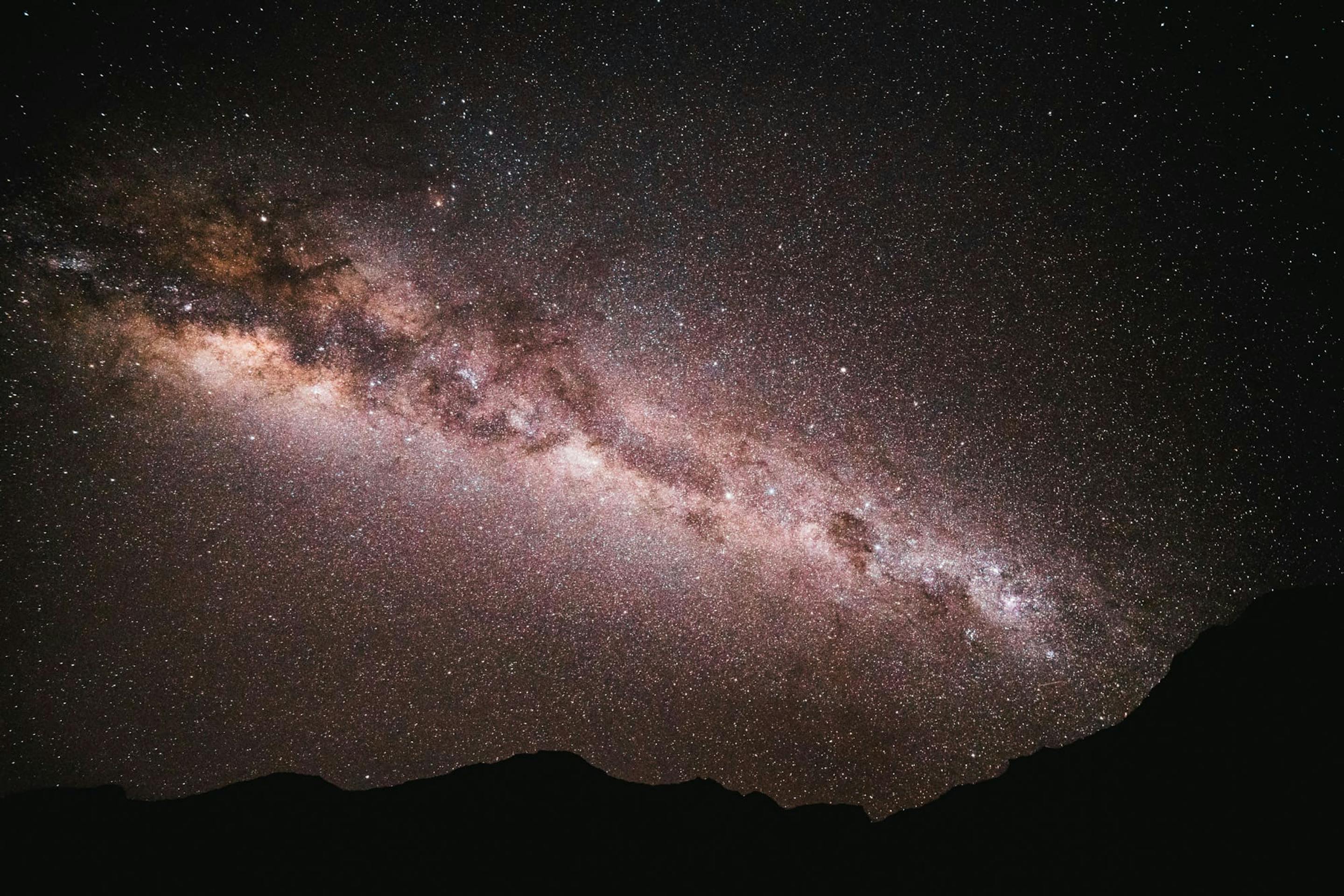 The Milky Way arches across a dark Atacama sky, with dense stars above the low silhouette of distant hills.