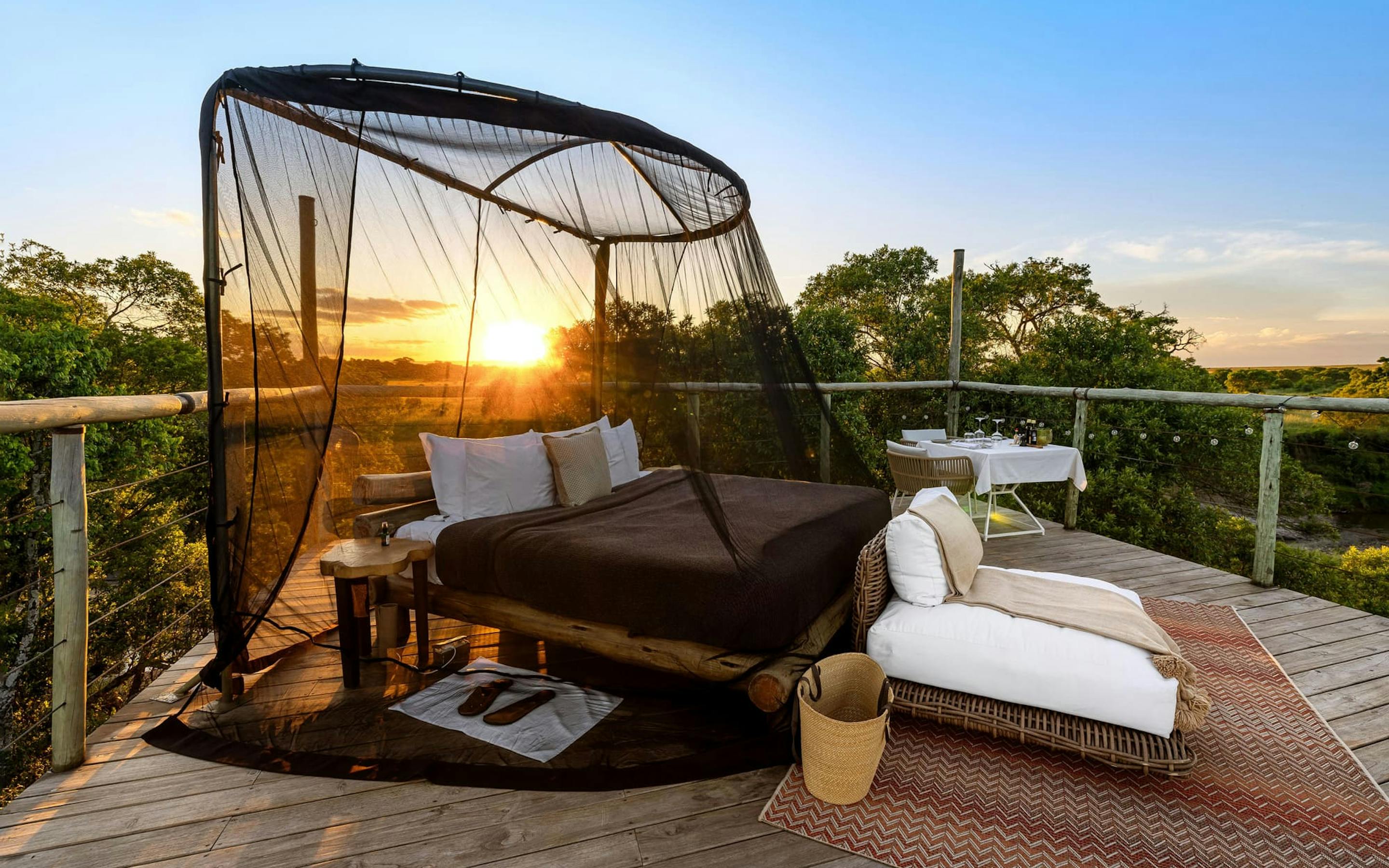 A starbed with a net canopy faces sunrise on a raised deck, overlooking the wide Masai Mara plains below.