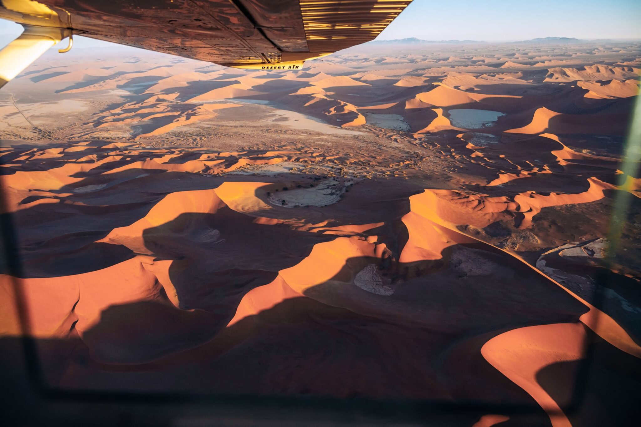 Aerial view of towering red sand dunes and deep shadows, seen from a plane as the desert curves away below.
