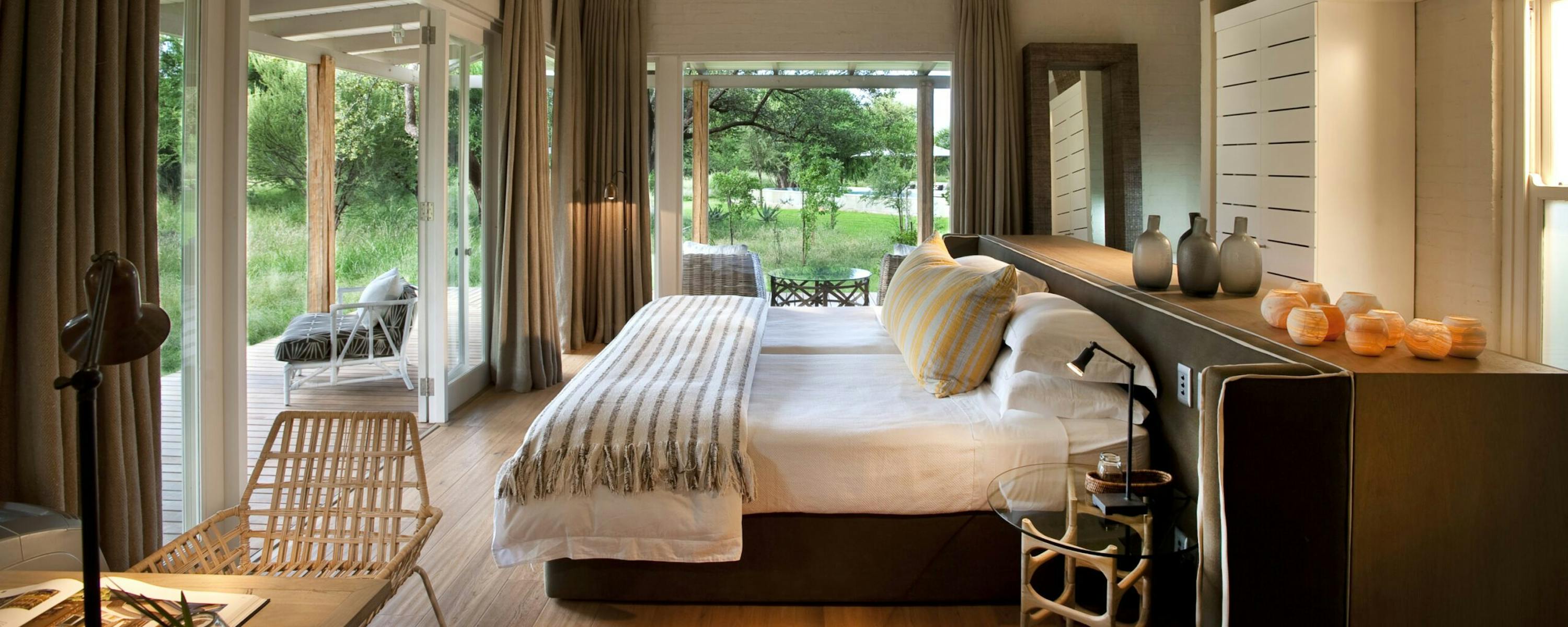 Bright bedroom with twin beds and white rafters opens to garden views through wide glass doors and soft curtains.
