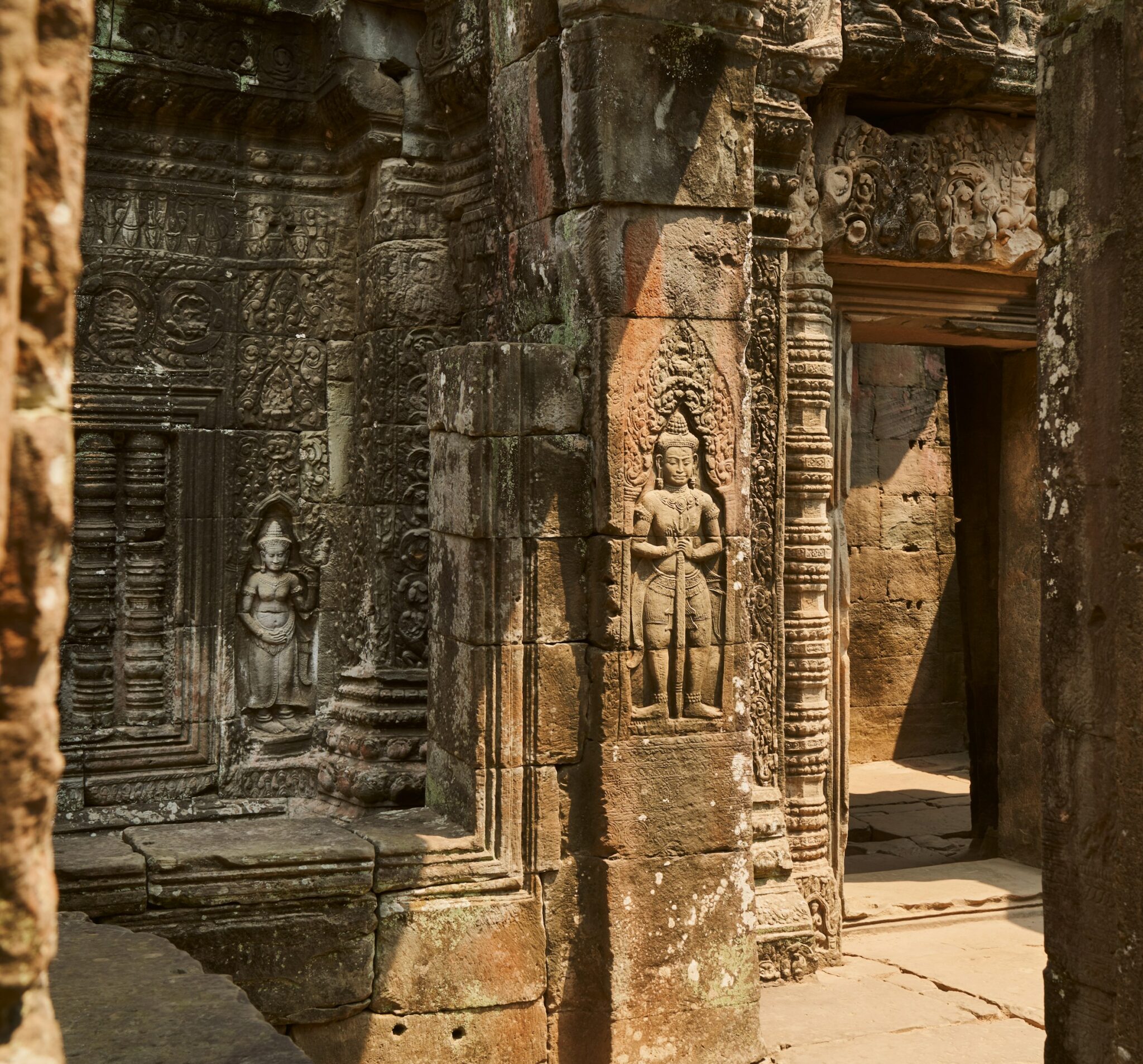 Sunlit stone carvings frame a temple doorway, with weathered columns and reliefs in warm afternoon light.