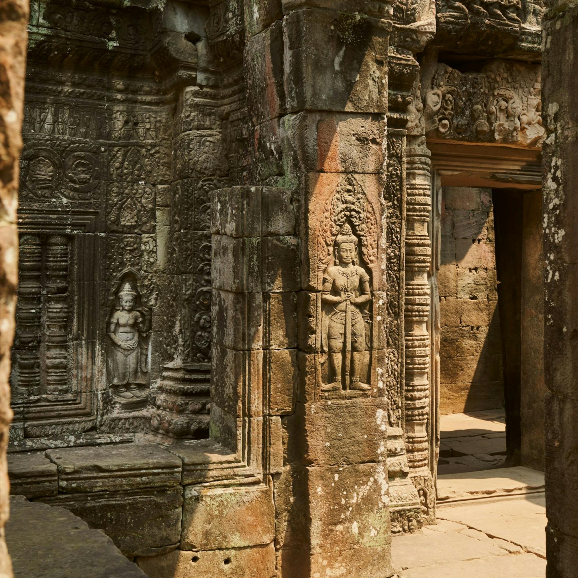 Sunlit stone carvings frame a temple doorway, with weathered columns and reliefs in warm afternoon light.