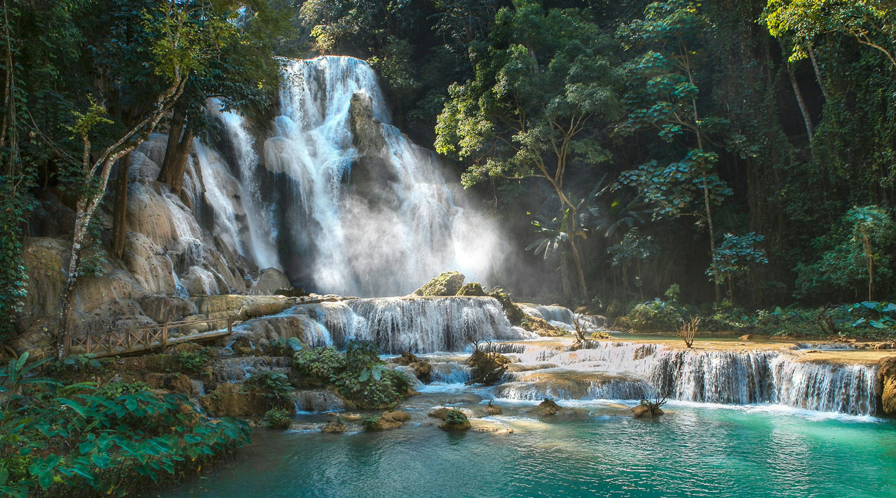 A multi-tiered waterfall spills into bright turquoise pools surrounded by dense jungle foliage and mossy rocks.