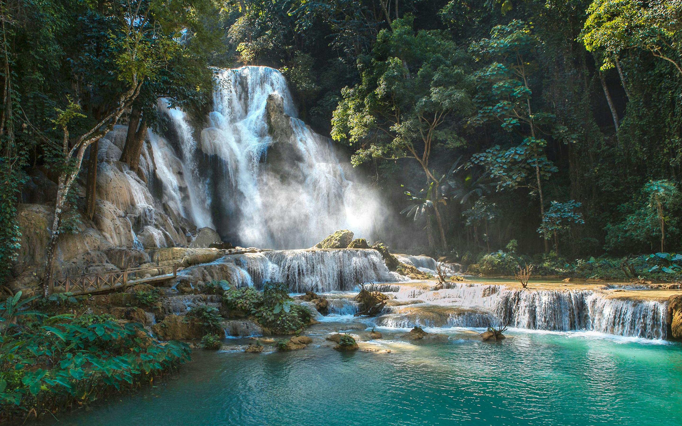 A multi-tiered waterfall spills into bright turquoise pools surrounded by dense jungle foliage and mossy rocks.