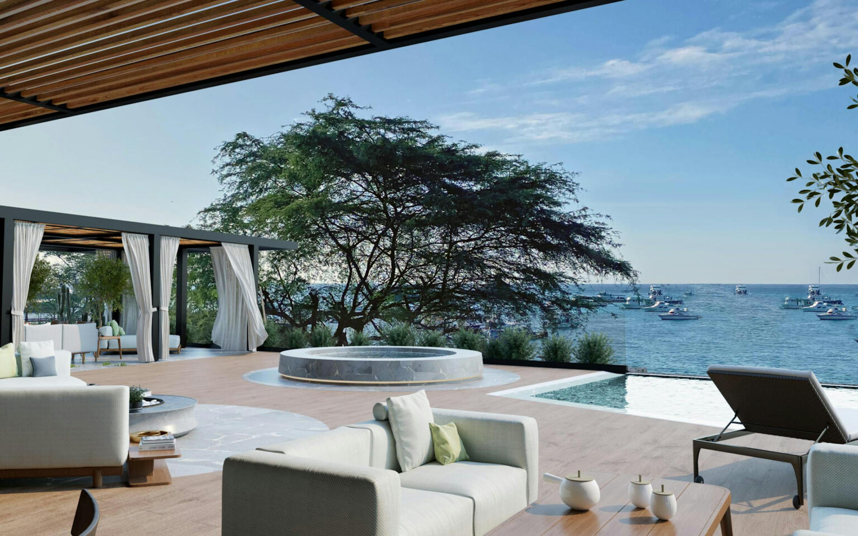 Modern terrace lounge with white sofas beside an infinity pool, looking out over calm ocean and anchored boats.