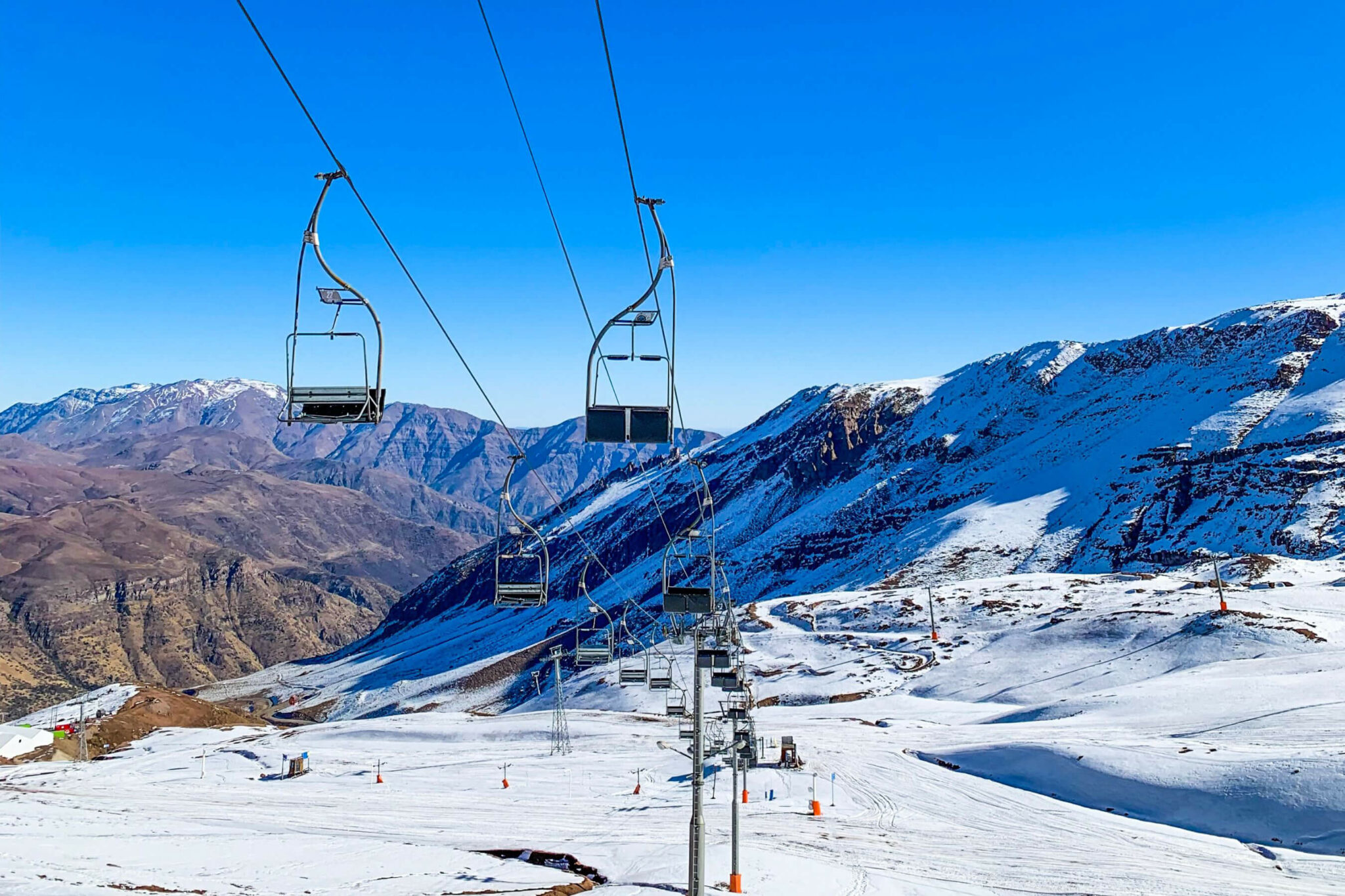 Empty ski chairs glide above snowy runs at Valle Nevado, framed by distant peaks and a deep, clear blue sky.