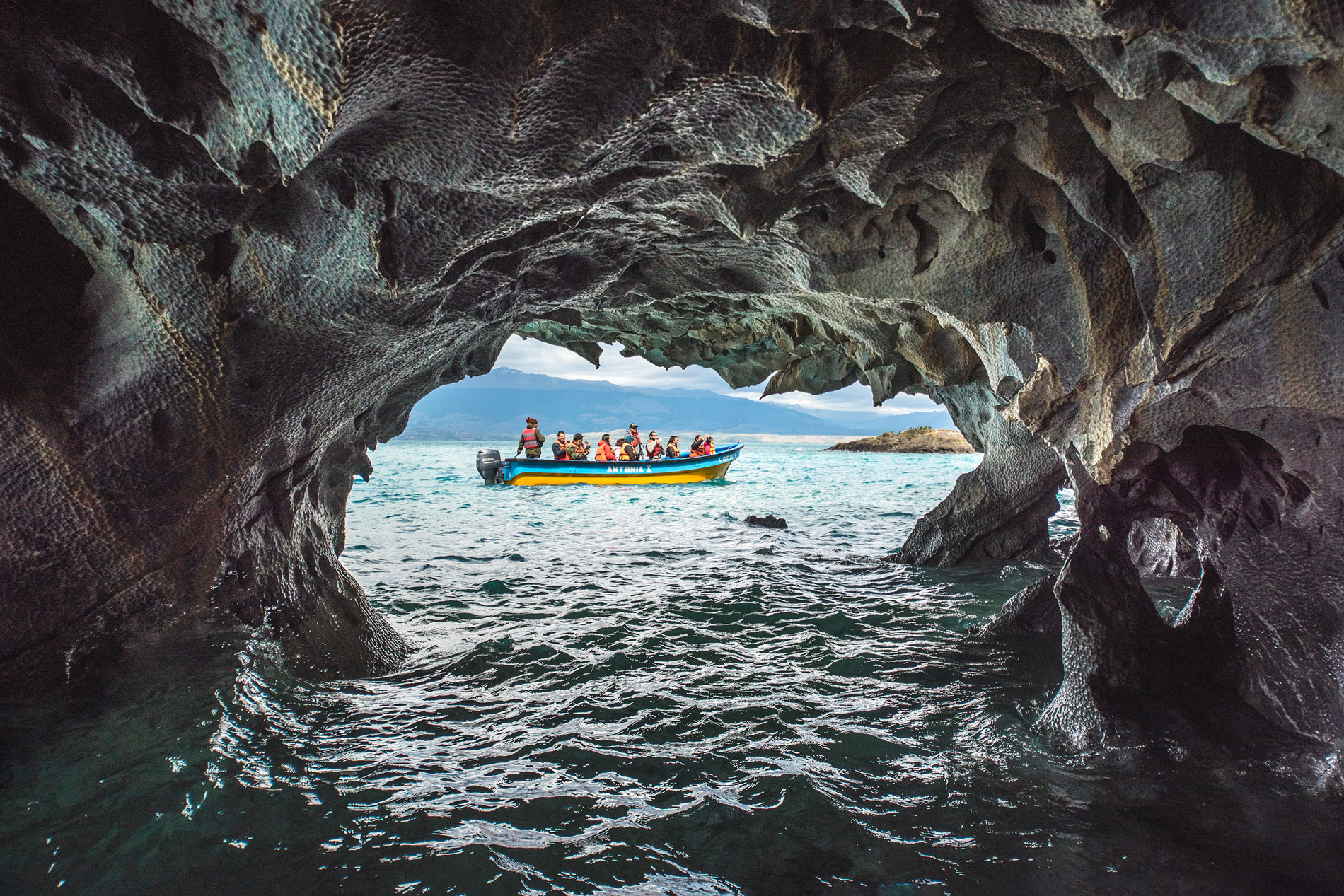 View from inside a dark cave opening onto bright turquoise water, with a small boat outside the cavern.