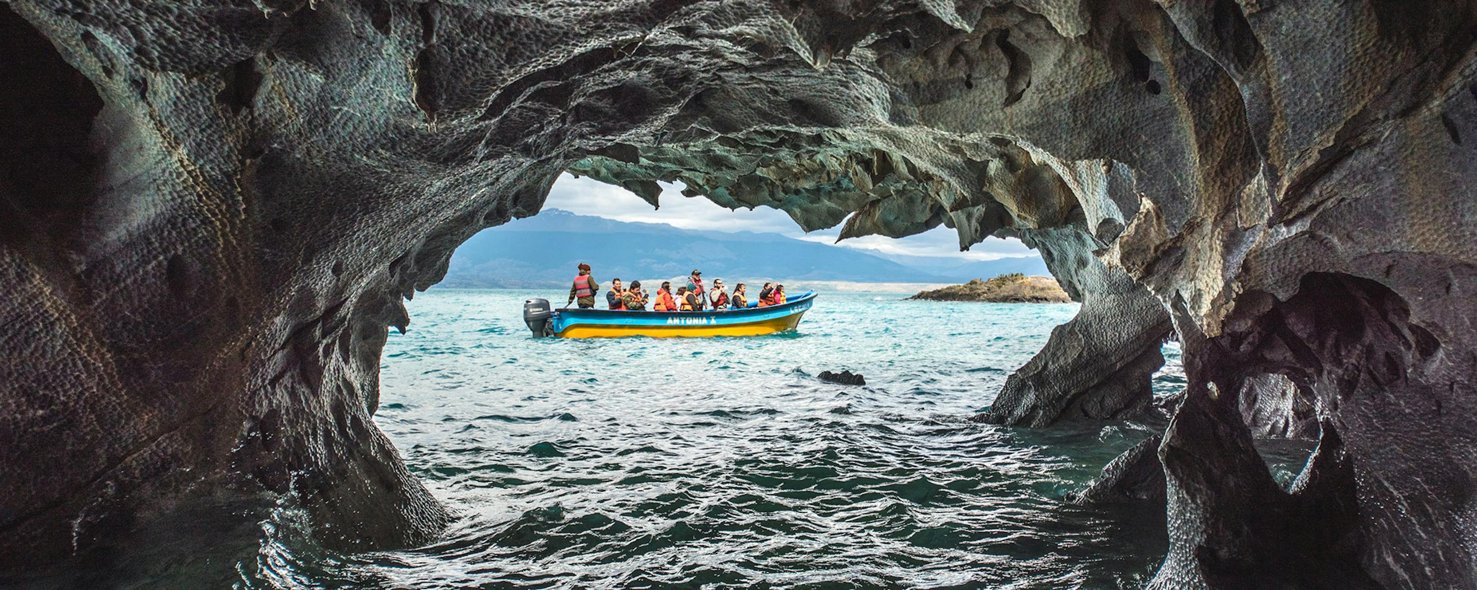 View from inside a dark cave opening onto bright turquoise water, with a small boat outside the cavern.