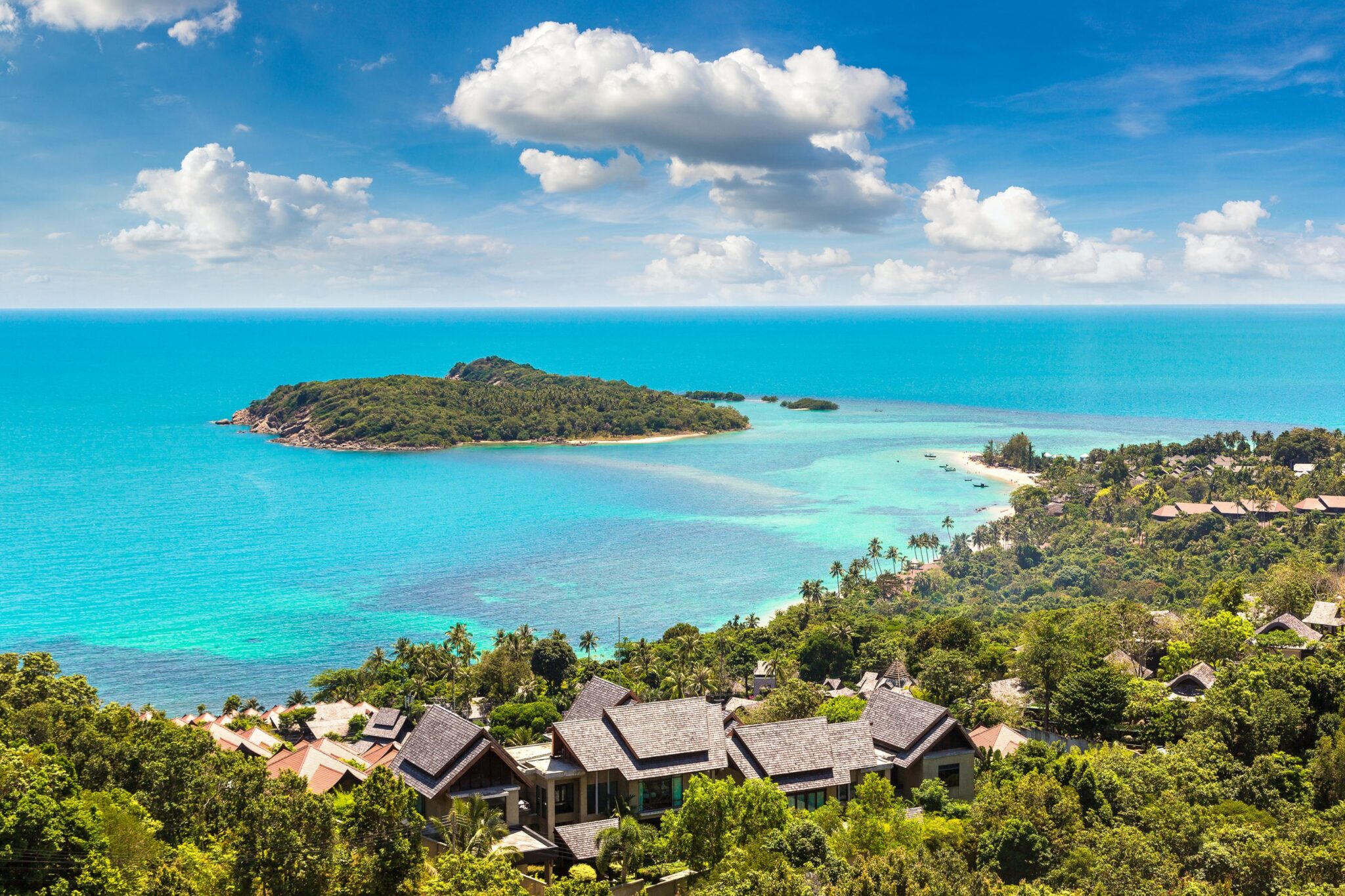 A tropical bay and offshore islets glow in turquoise water, with rooftops and palms spread across the hillside.