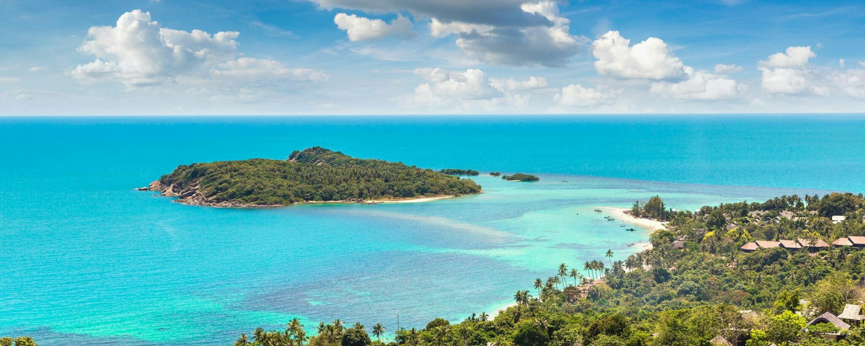 A tropical bay and offshore islets glow in turquoise water, with rooftops and palms spread across the hillside.
