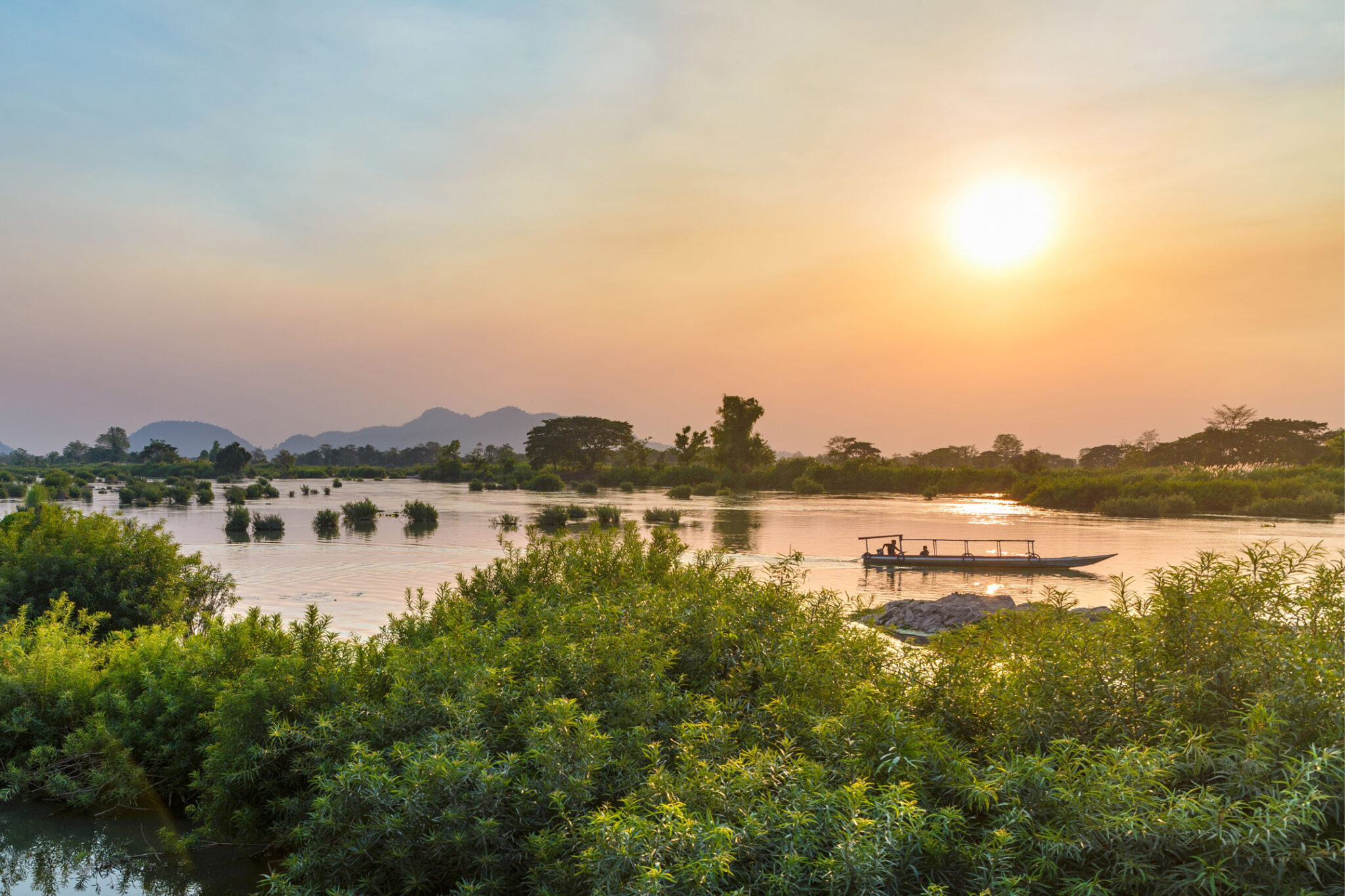 Golden sunset light reflects on the Mekong around the 4000 Islands, with silhouettes of trees and low islets.