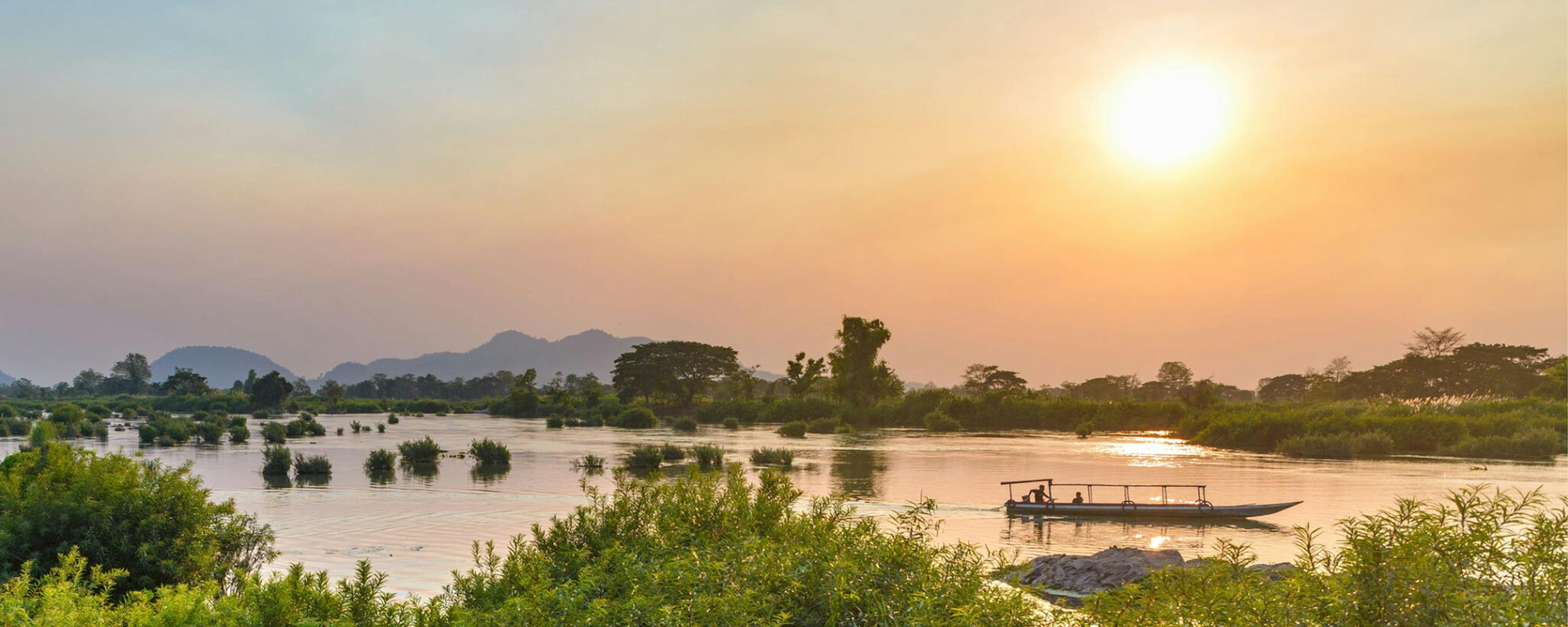 Golden sunset light reflects on the Mekong around the 4000 Islands, with silhouettes of trees and low islets.