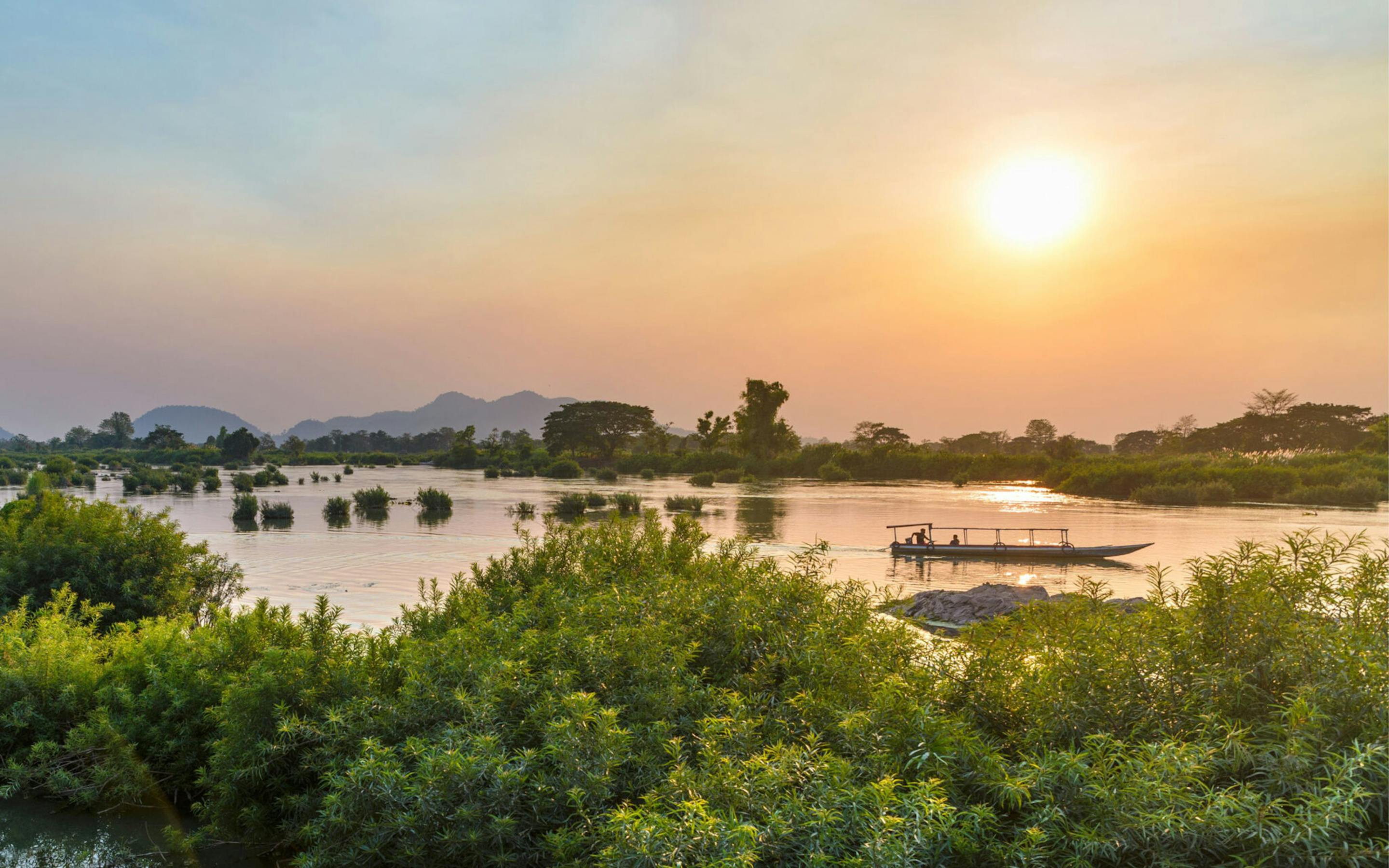 Golden sunset light reflects on the Mekong around the 4000 Islands, with silhouettes of trees and low islets.