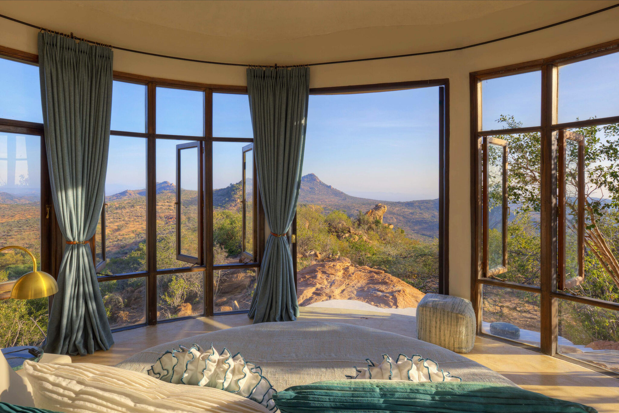 A soaking tub faces floor-to-ceiling windows, framing sunlit hills and a distant peak beneath a clear sky.
