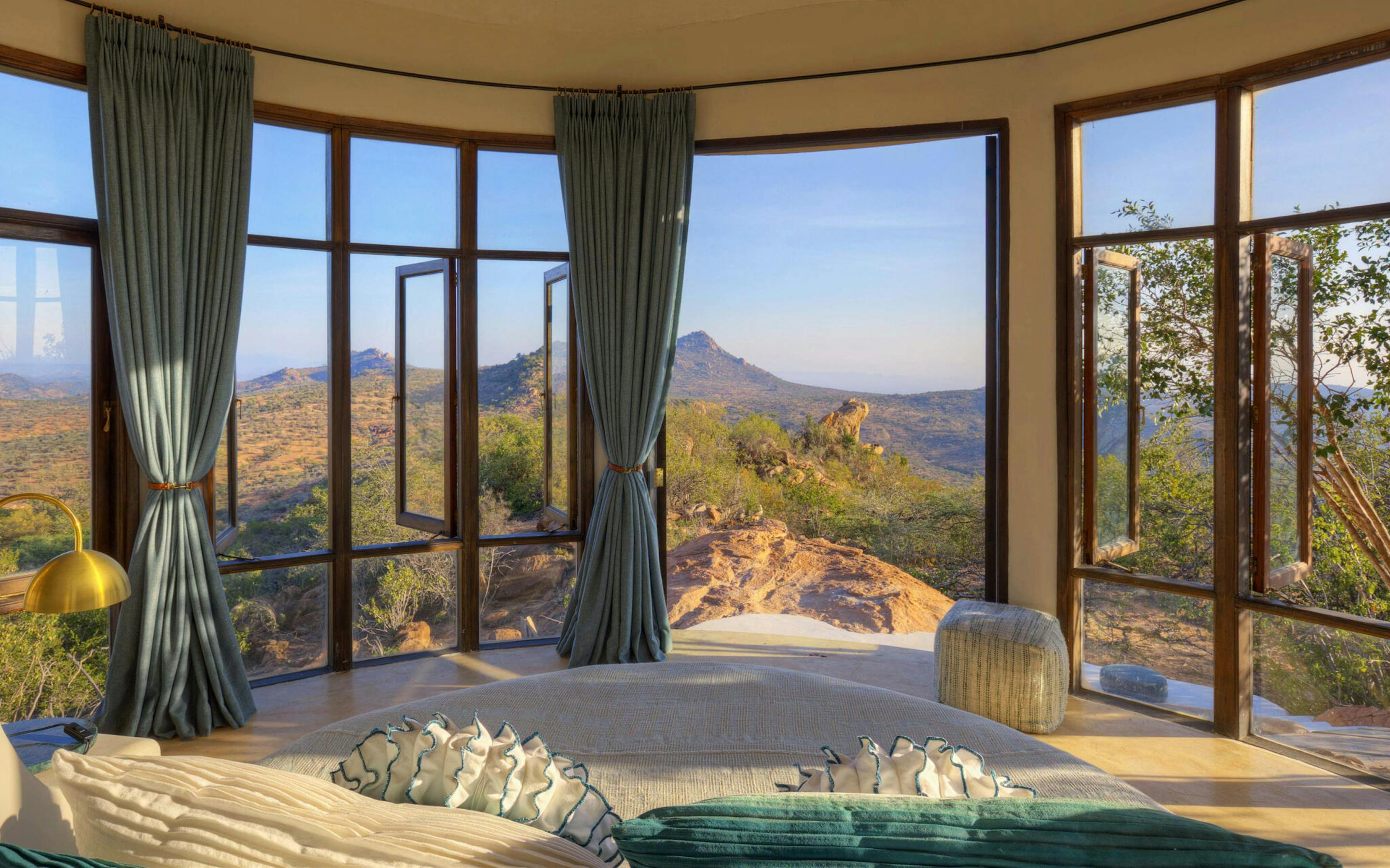 A soaking tub faces floor-to-ceiling windows, framing sunlit hills and a distant peak beneath a clear sky.